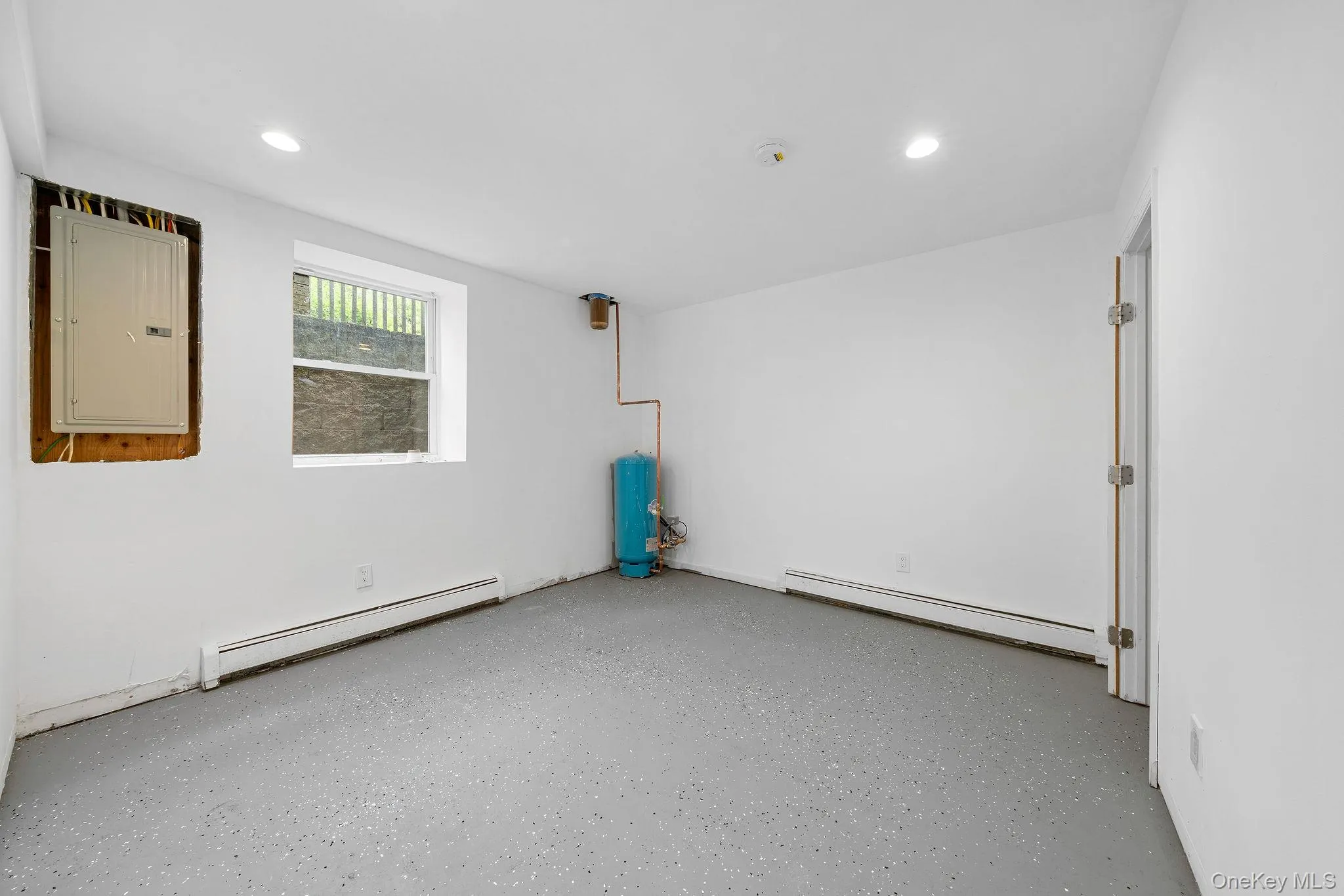 Brightly lit room featuring a window, white walls, and speckled flooring Brightly lit room featuring a window, white walls, and speckled flooring