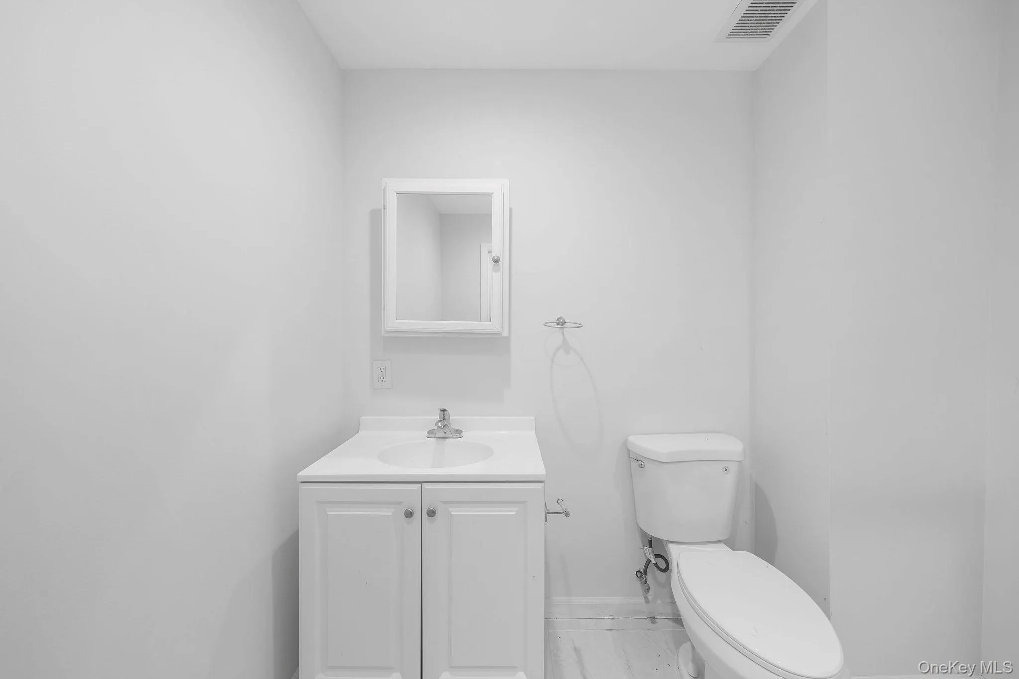 Bathroom featuring a white vanity with integrated sink, chrome faucet, white medicine cabinet, and a toilet Bathroom featuring a white vanity with integrated sink, chrome faucet, white medicine cabinet, and a toilet