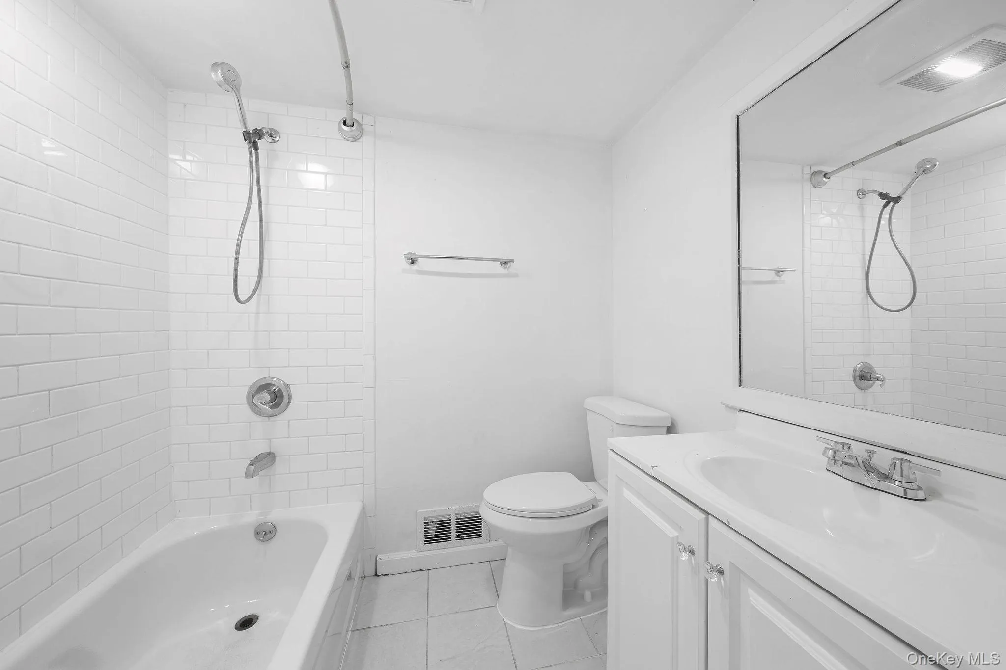 Bathroom featuring white subway tile surround, chrome fixtures, a single vanity with storage, and a large wall-mounted mirror Bathroom featuring white subway tile surround, chrome fixtures, a single vanity with storage, and a large wall-mounted mirror