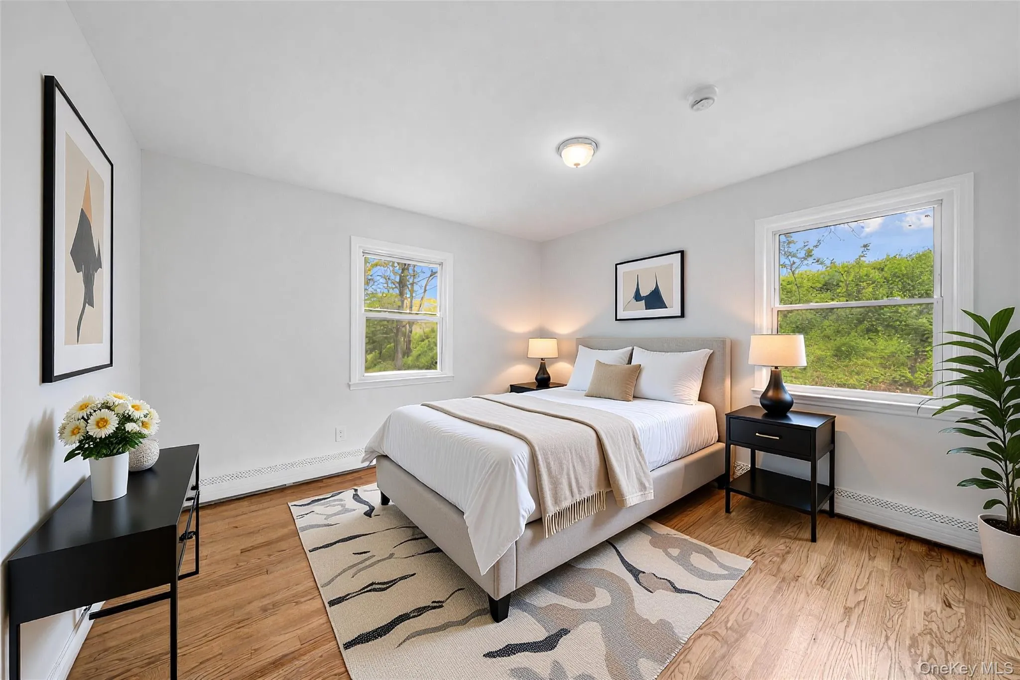 Bedroom featuring wood-finish flooring, light grey walls, and two single-hung windows. Image is Virtually Staged. Bedroom featuring wood-finish flooring, light grey walls, and two single-hung windows. Image is Virtually Staged.
