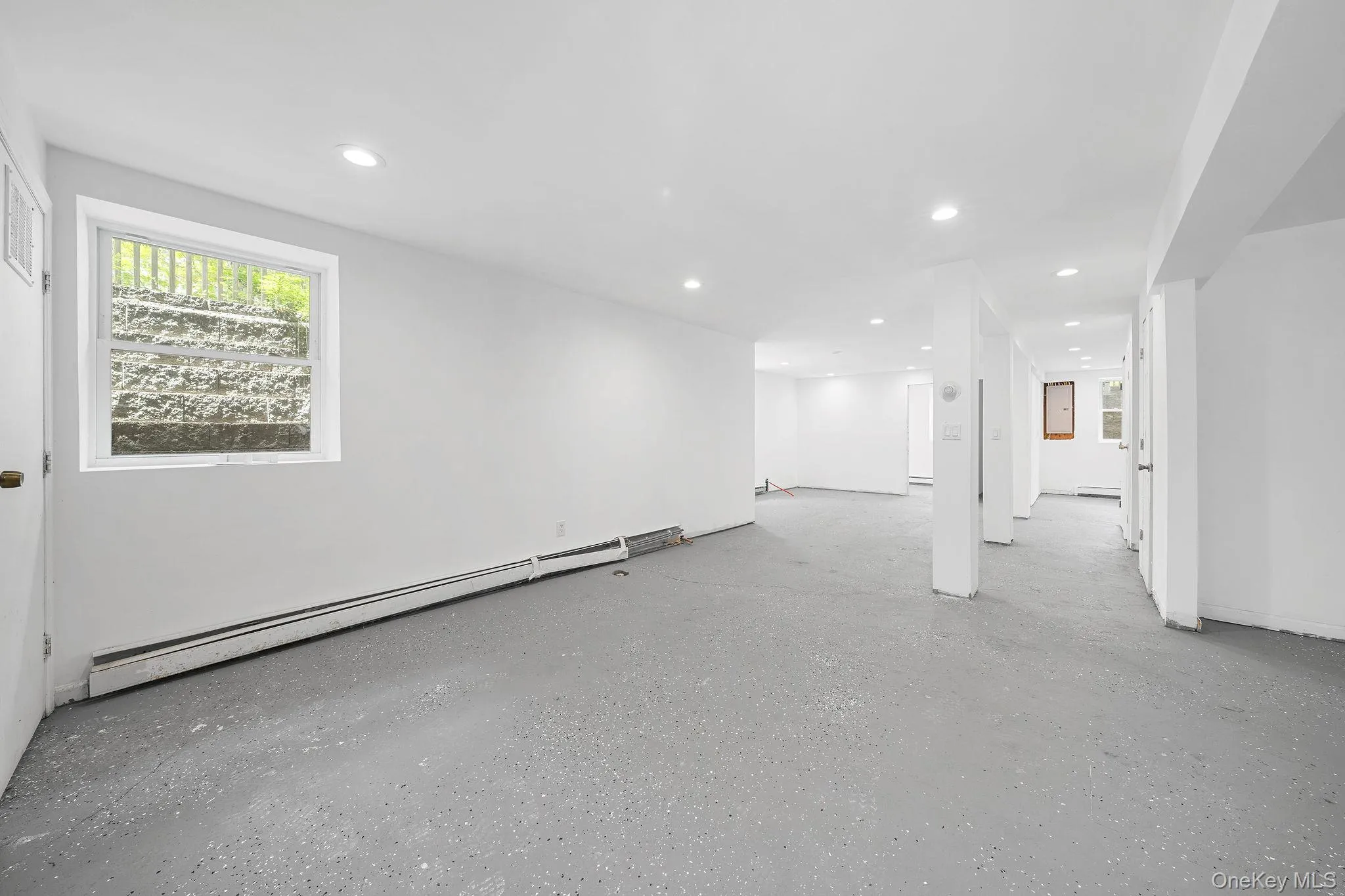 Spacious lower-level area featuring white walls, recessed lighting, and a durable gray speckled floor Spacious lower-level area featuring white walls, recessed lighting, and a durable gray speckled floor