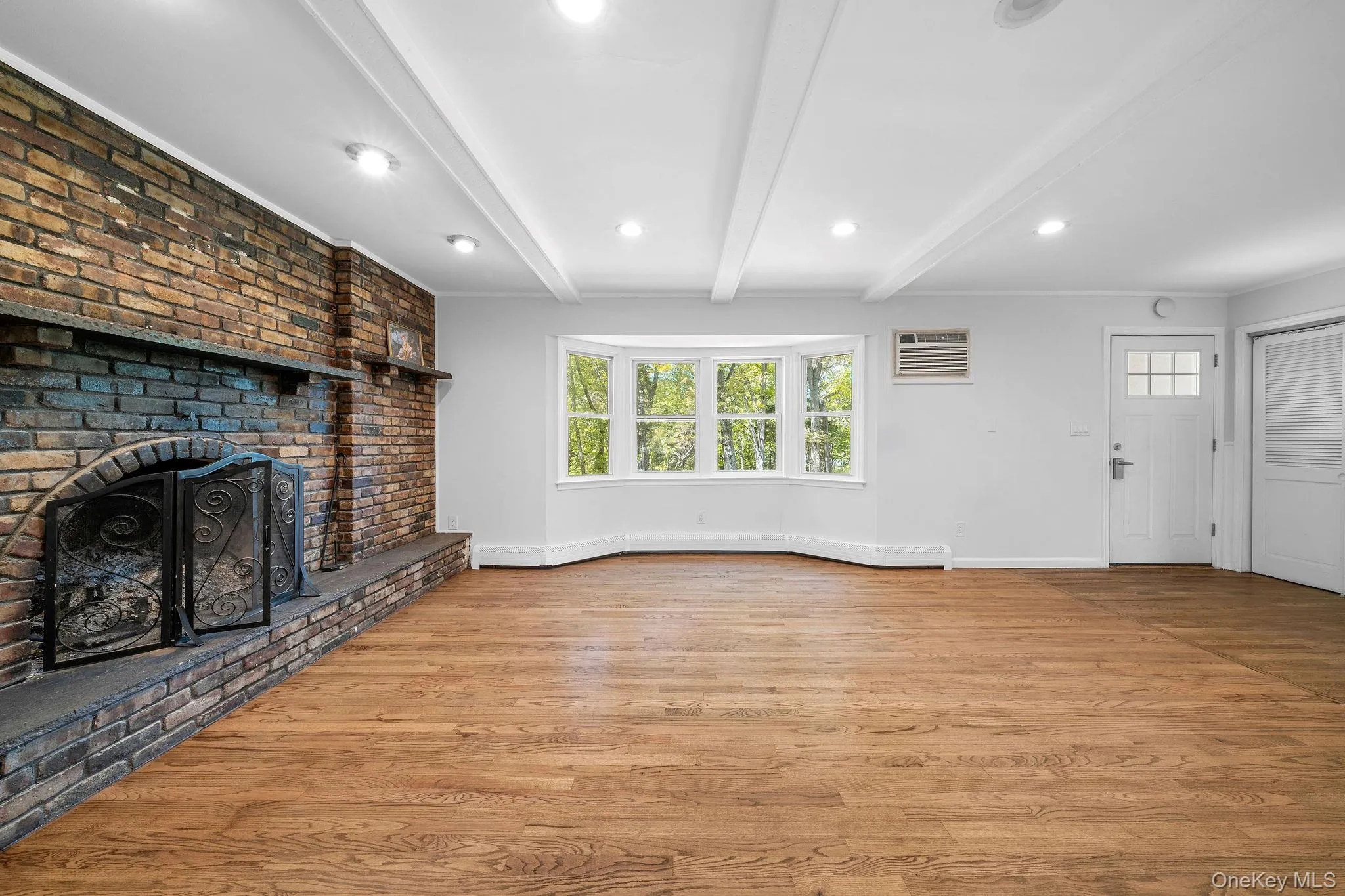 Exposed brick fireplace with a stone hearth, wood-finish flooring, and a bay window Exposed brick fireplace with a stone hearth, wood-finish flooring, and a bay window