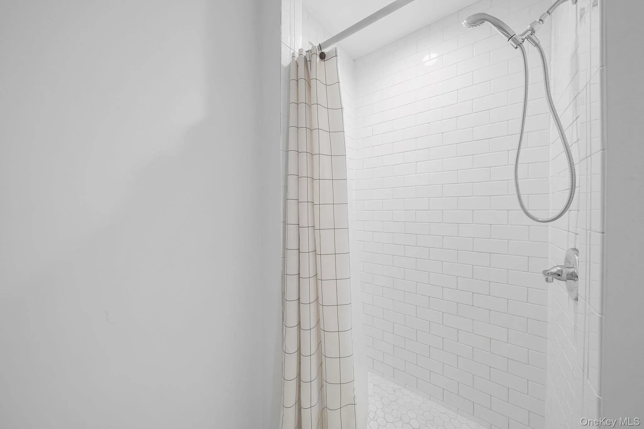 Shower with white subway tile walls, chrome fixtures, and a hexagon-tiled floor Shower with white subway tile walls, chrome fixtures, and a hexagon-tiled floor