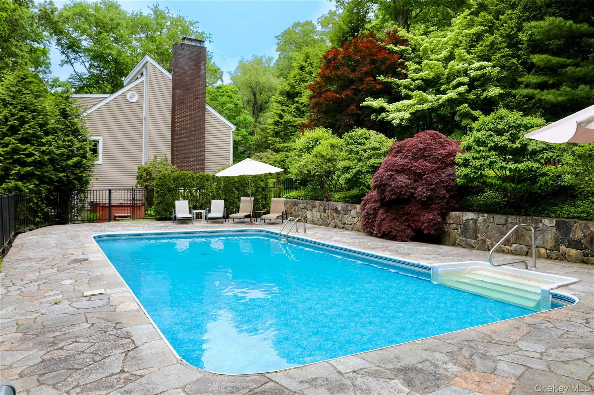 Inground pool with stone patio surrounded by mature landscaping Inground pool with stone patio surrounded by mature landscaping