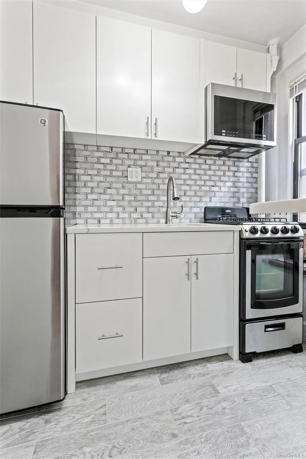 Renovated modern kitchen featuring stainless steel appliances, white cabinetry, and a textured backsplash. Renovated modern kitchen featuring stainless steel appliances, white cabinetry, and a textured backsplash.