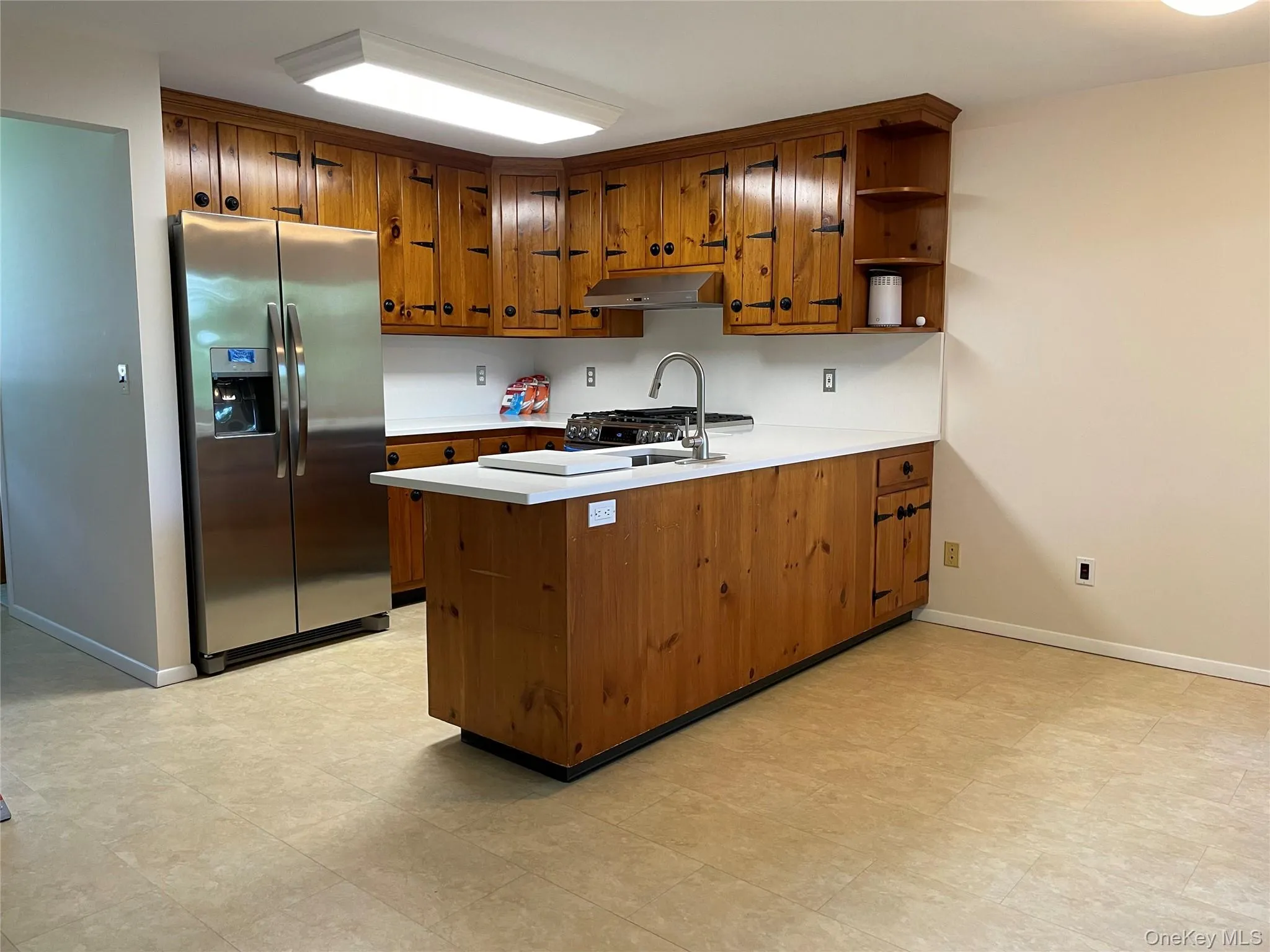 Eat-in Kitchen featuring stainless steel refrigerator with ice dispenser, under cabinet range hood, a peninsula, brown cabinets, and quartz countertops Eat-in Kitchen featuring stainless steel refrigerator with ice dispenser, under cabinet range hood, a peninsula, brown cabinets, and quartz countertops