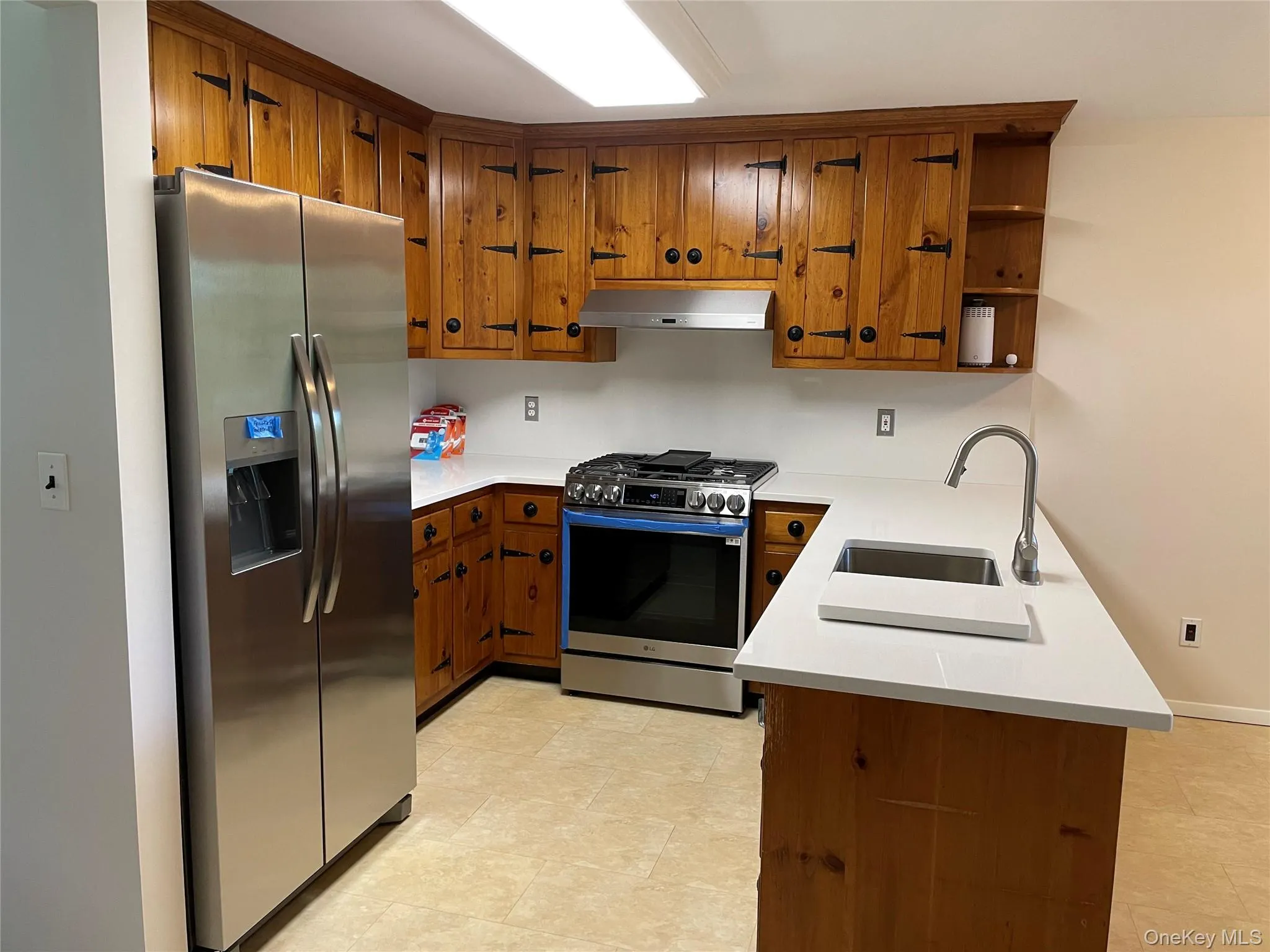 Kitchen with stainless steel appliances, range hood, brown cabinetry, light countertops, and a peninsula Kitchen with stainless steel appliances, range hood, brown cabinetry, light countertops, and a peninsula