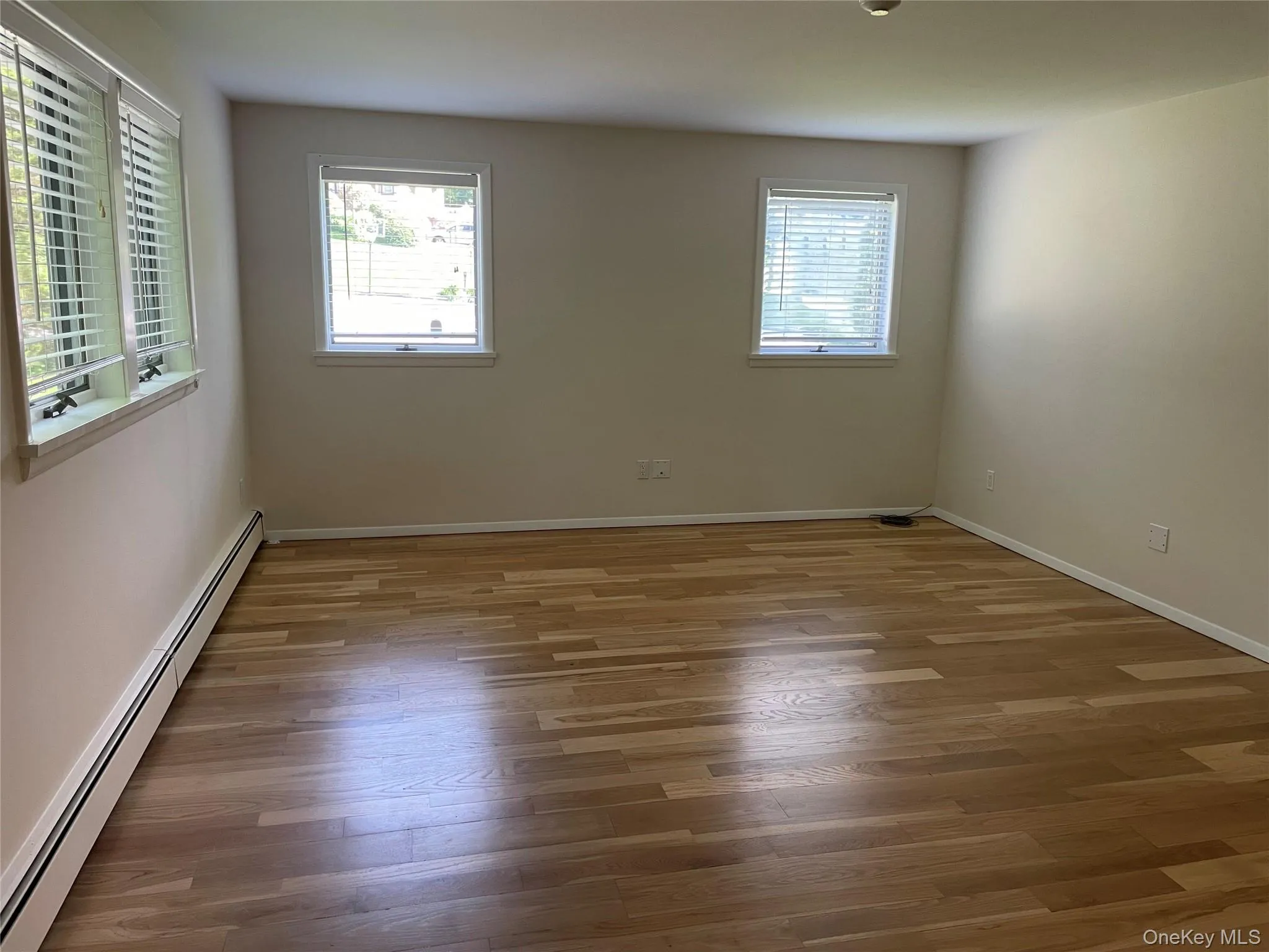 Spare room with baseboard heating, plenty of natural light, and wood finished floors Spare room with baseboard heating, plenty of natural light, and wood finished floors