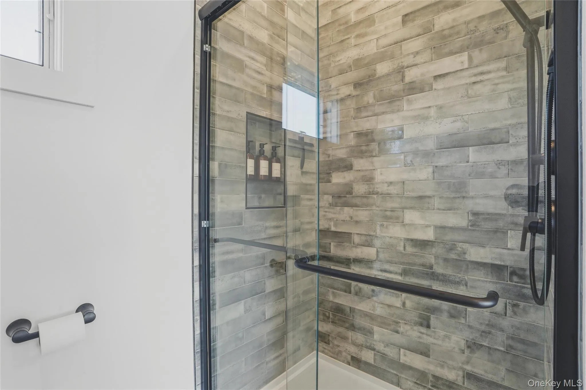 Glass-enclosed shower with matte black hardware, textured tile surround, and an integrated shower niche Glass-enclosed shower with matte black hardware, textured tile surround, and an integrated shower niche