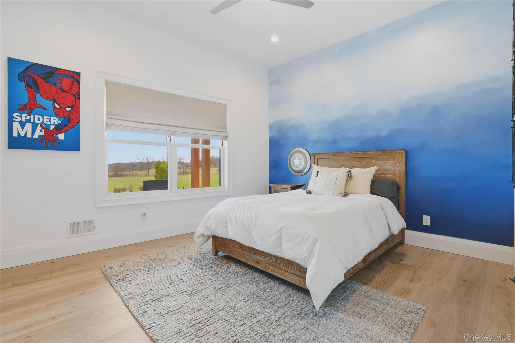 Bedroom featuring a broad window with expansive outdoor scenery, a distinctive blue gradient accent wall, wood-finish flooring, and a ceiling fan Bedroom featuring a broad window with expansive outdoor scenery, a distinctive blue gradient accent wall, wood-finish flooring, and a ceiling fan