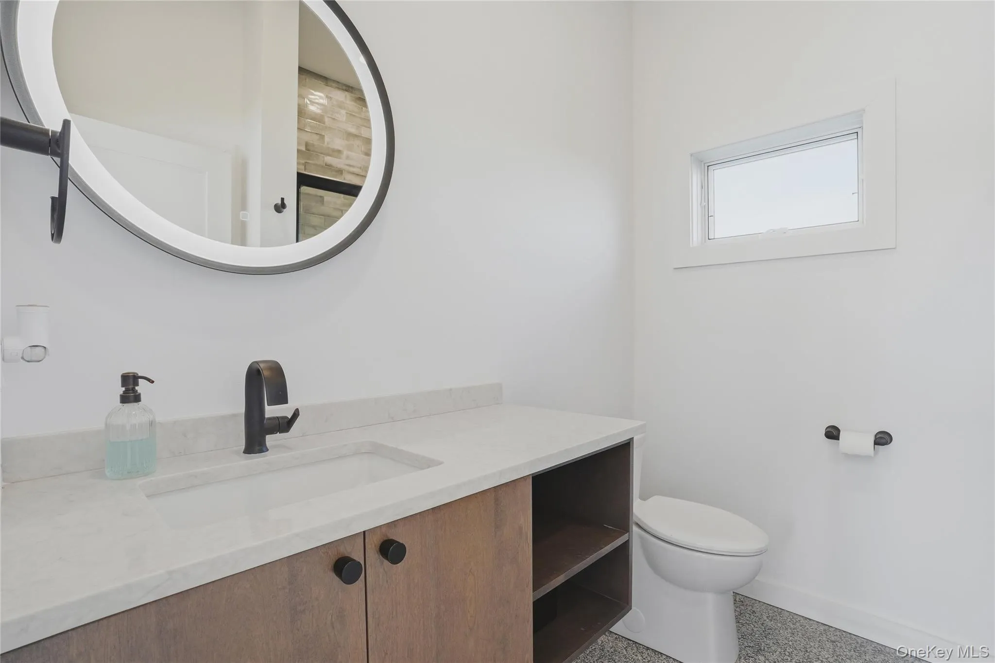 Bathroom featuring a wood-finish vanity with an integrated sink, light-toned countertop, and matte black faucet Bathroom featuring a wood-finish vanity with an integrated sink, light-toned countertop, and matte black faucet