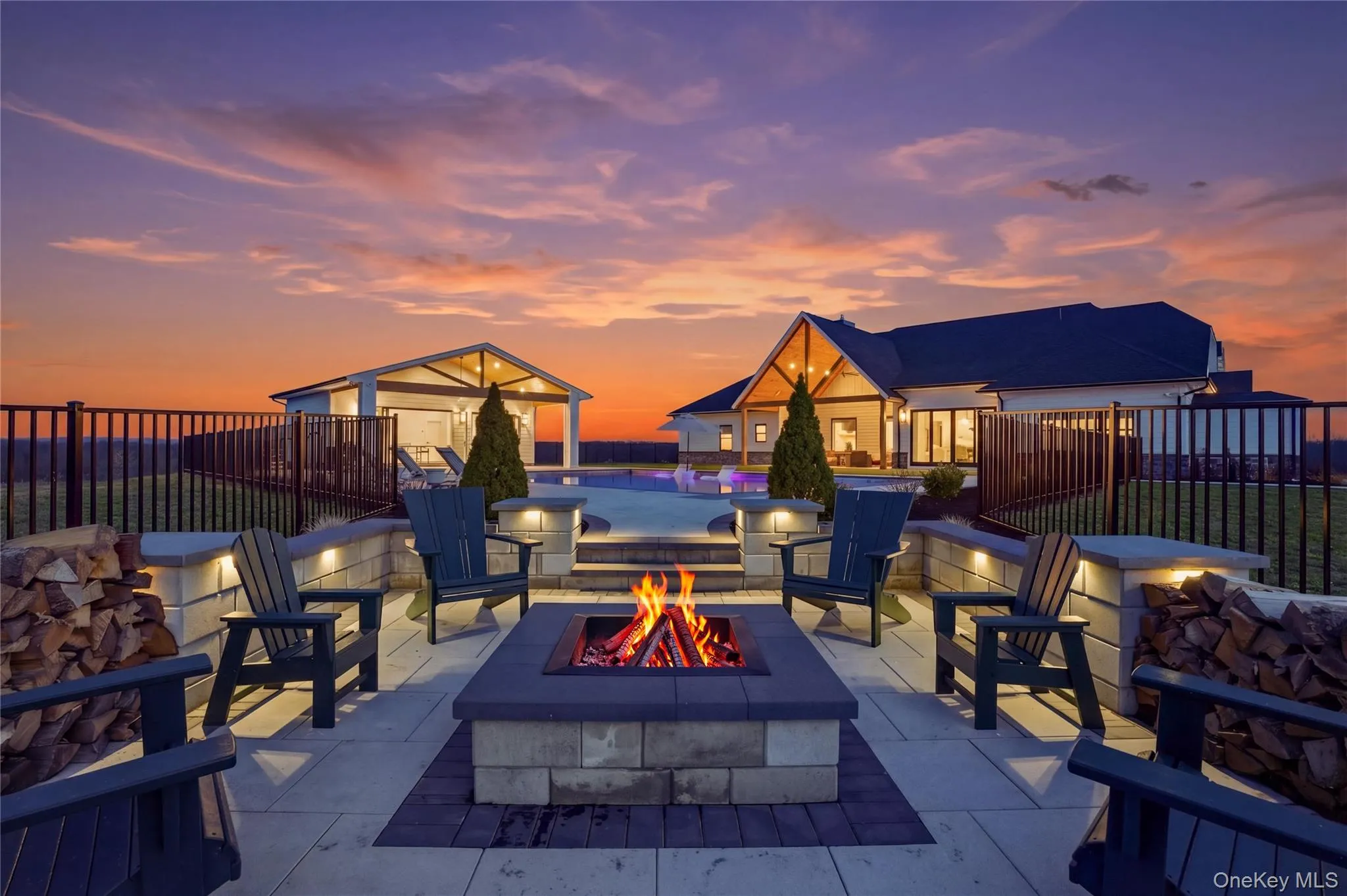 Outdoor patio area featuring a built-in fire pit, stone retaining walls with integrated lighting, and paver flooring Outdoor patio area featuring a built-in fire pit, stone retaining walls with integrated lighting, and paver flooring