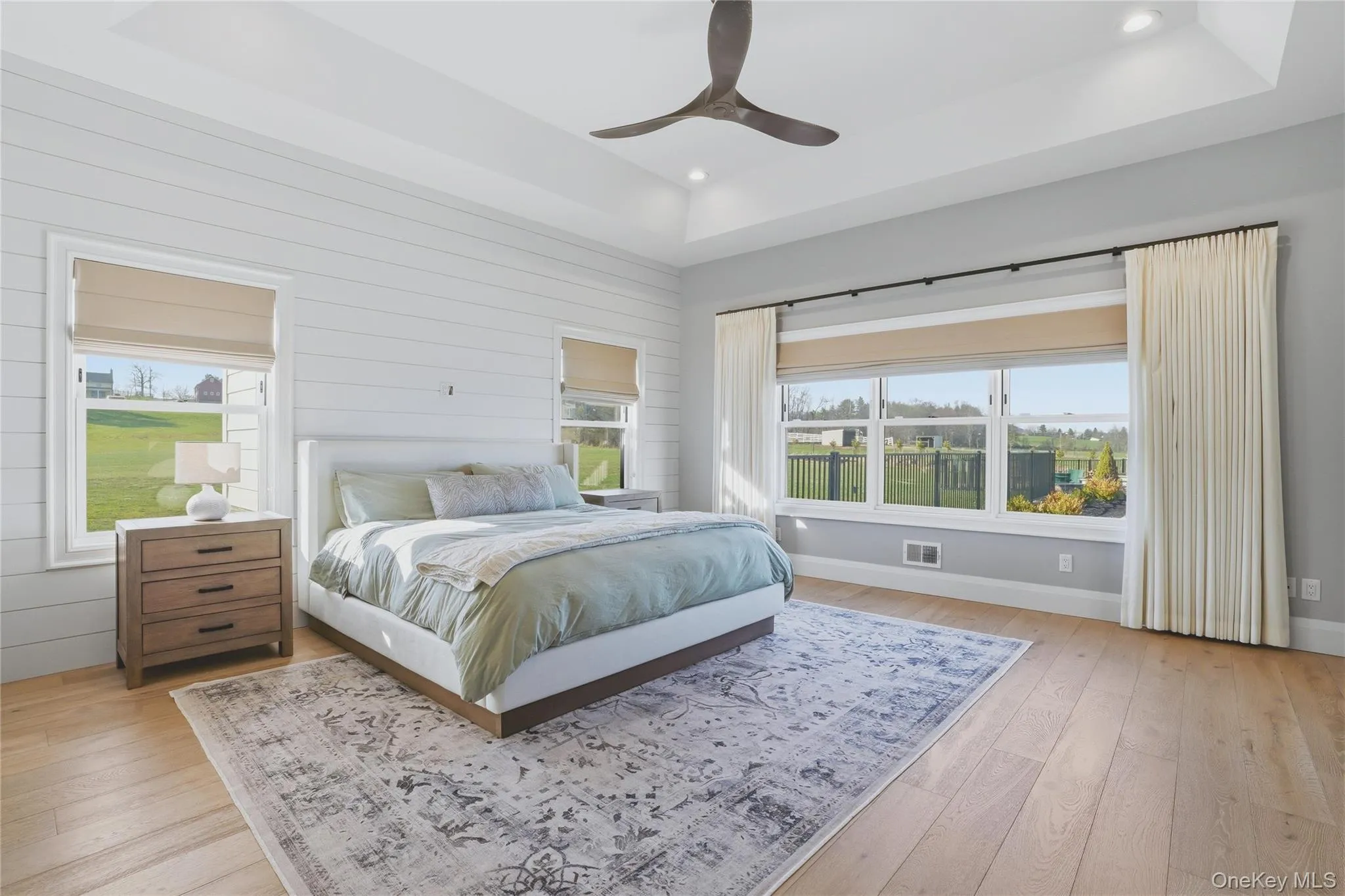 Spacious bedroom featuring light wood-finish flooring, a tray ceiling, recessed lighting, and a modern ceiling fan Spacious bedroom featuring light wood-finish flooring, a tray ceiling, recessed lighting, and a modern ceiling fan