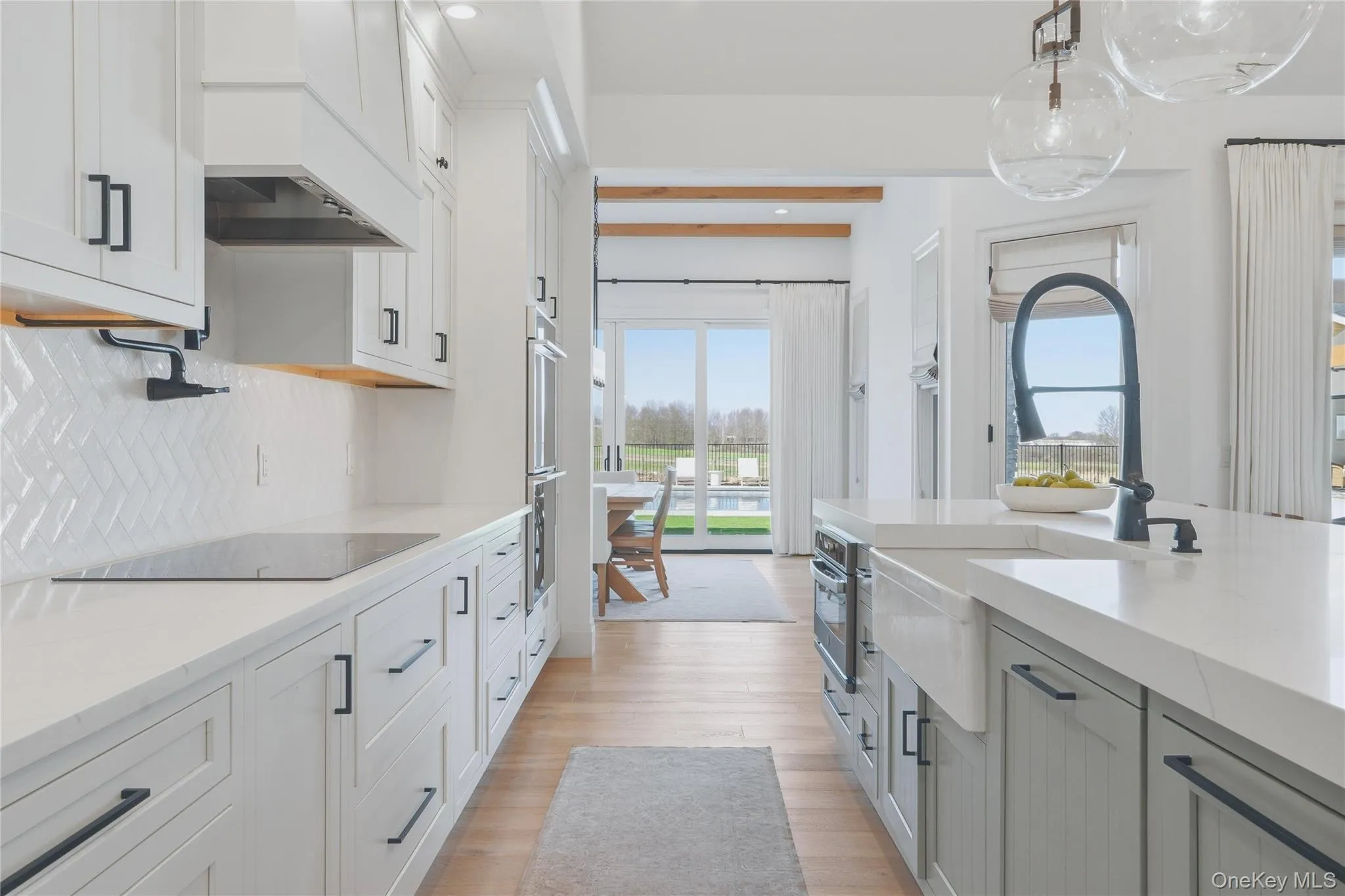 Modern kitchen featuring white cabinetry with matte black hardware, white herringbone tile backsplash, and light wood-finish flooring Modern kitchen featuring white cabinetry with matte black hardware, white herringbone tile backsplash, and light wood-finish flooring