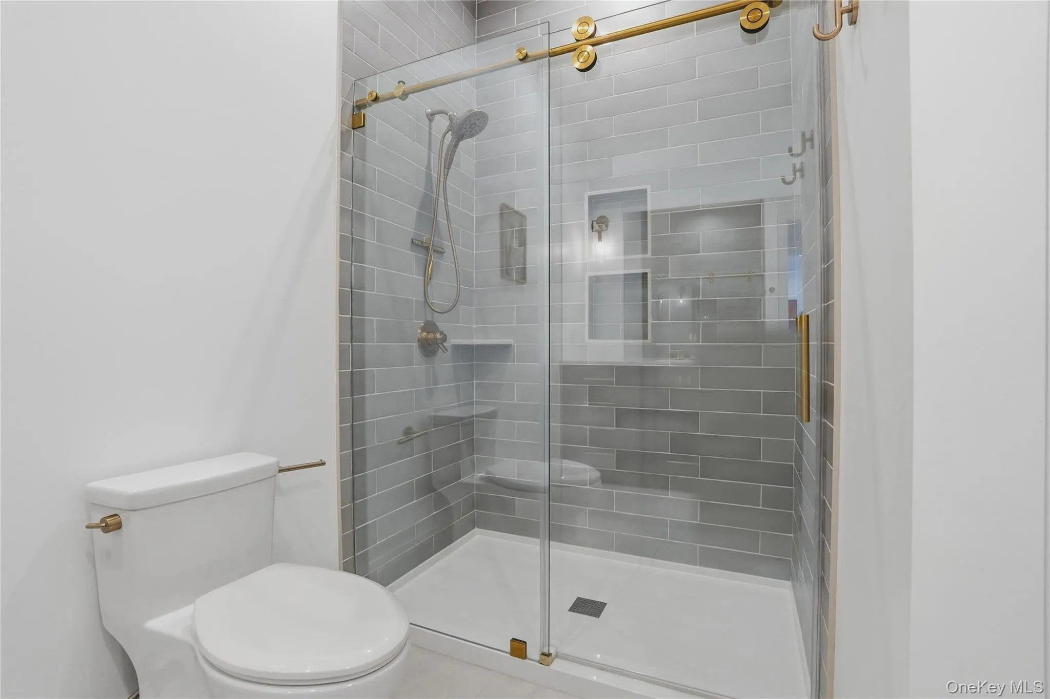 Walk-in shower with clear glass enclosure and gold-toned hardware, featuring light gray subway tile Walk-in shower with clear glass enclosure and gold-toned hardware, featuring light gray subway tile