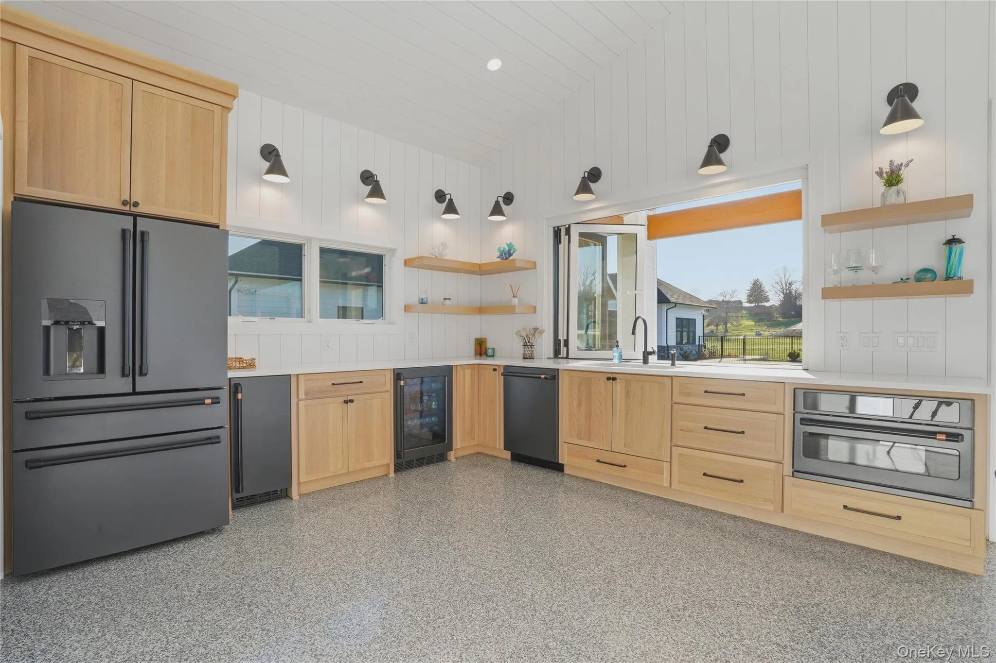 Modern kitchen featuring light wood cabinetry, a large matte black refrigerator, and an expansive pass-through window Modern kitchen featuring light wood cabinetry, a large matte black refrigerator, and an expansive pass-through window