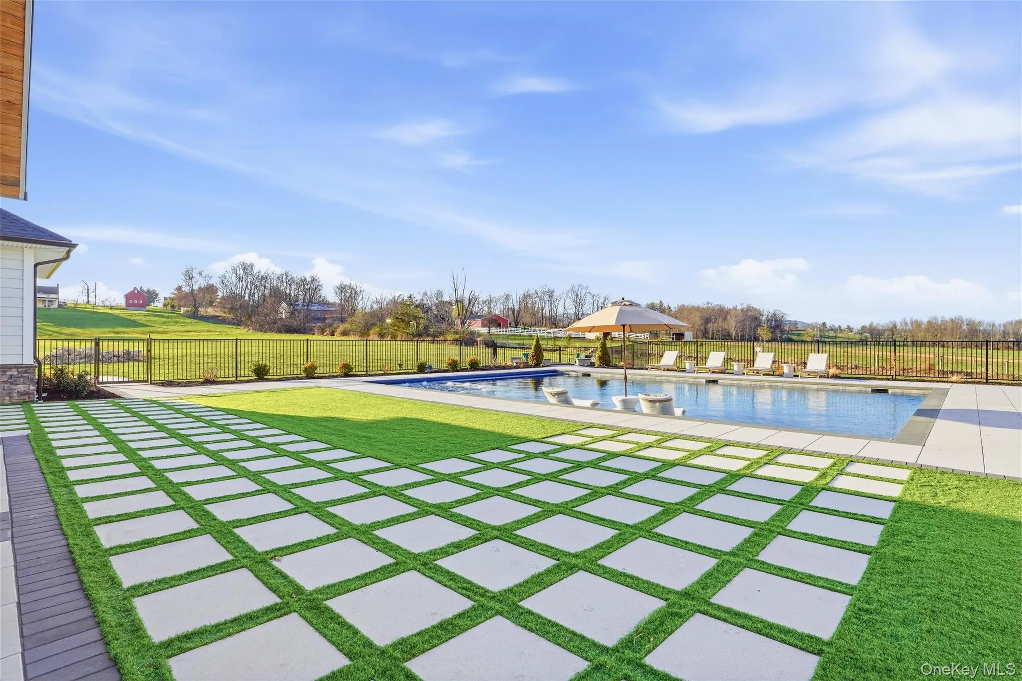 Expansive outdoor living area featuring a rectangular swimming pool, integrated sun loungers, and a paved patio with grass inlays Expansive outdoor living area featuring a rectangular swimming pool, integrated sun loungers, and a paved patio with grass inlays