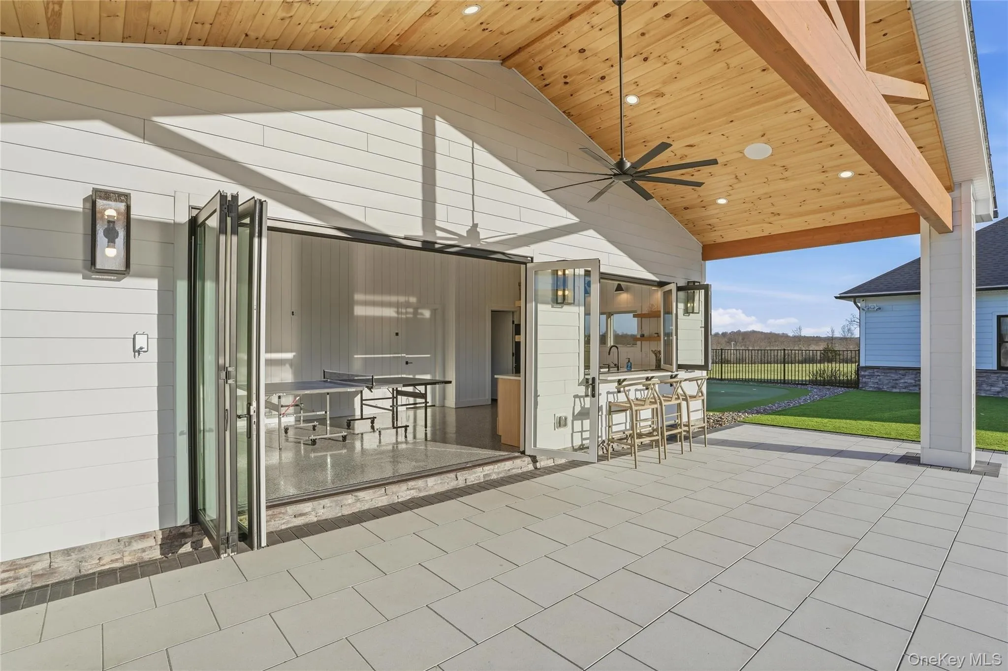 Expansive outdoor living area featuring a wood-finished vaulted ceiling, overhead fan, recessed lighting, and a built-in bar with bifold windows Expansive outdoor living area featuring a wood-finished vaulted ceiling, overhead fan, recessed lighting, and a built-in bar with bifold windows