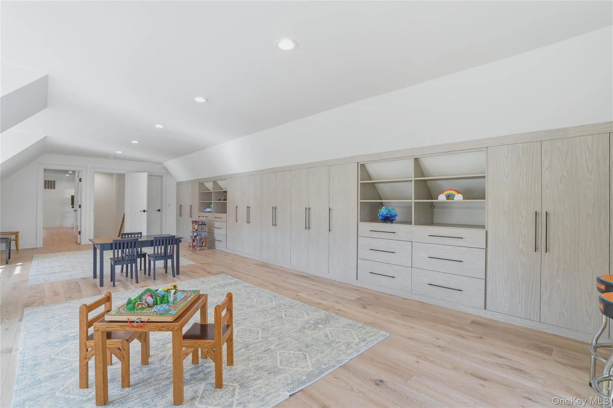 Spacious room featuring extensive built-in cabinetry with integrated shelving and drawers, light wood-finish flooring, recessed lighting, and white walls Spacious room featuring extensive built-in cabinetry with integrated shelving and drawers, light wood-finish flooring, recessed lighting, and white walls