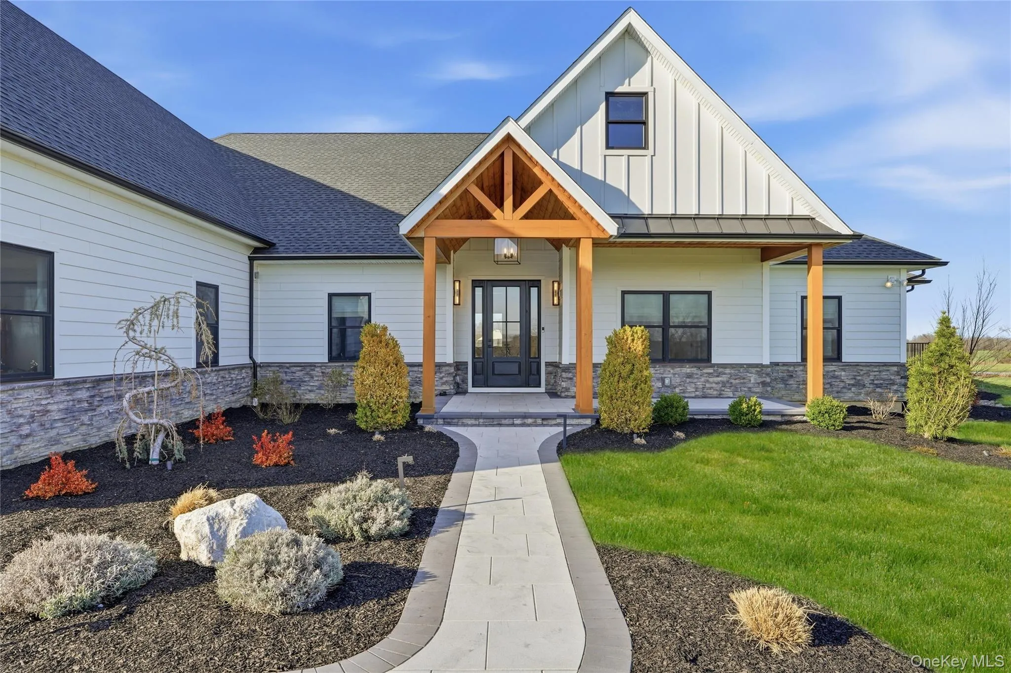 Modern farmhouse exterior featuring white siding, a dark roof, and stone facade accents Modern farmhouse exterior featuring white siding, a dark roof, and stone facade accents