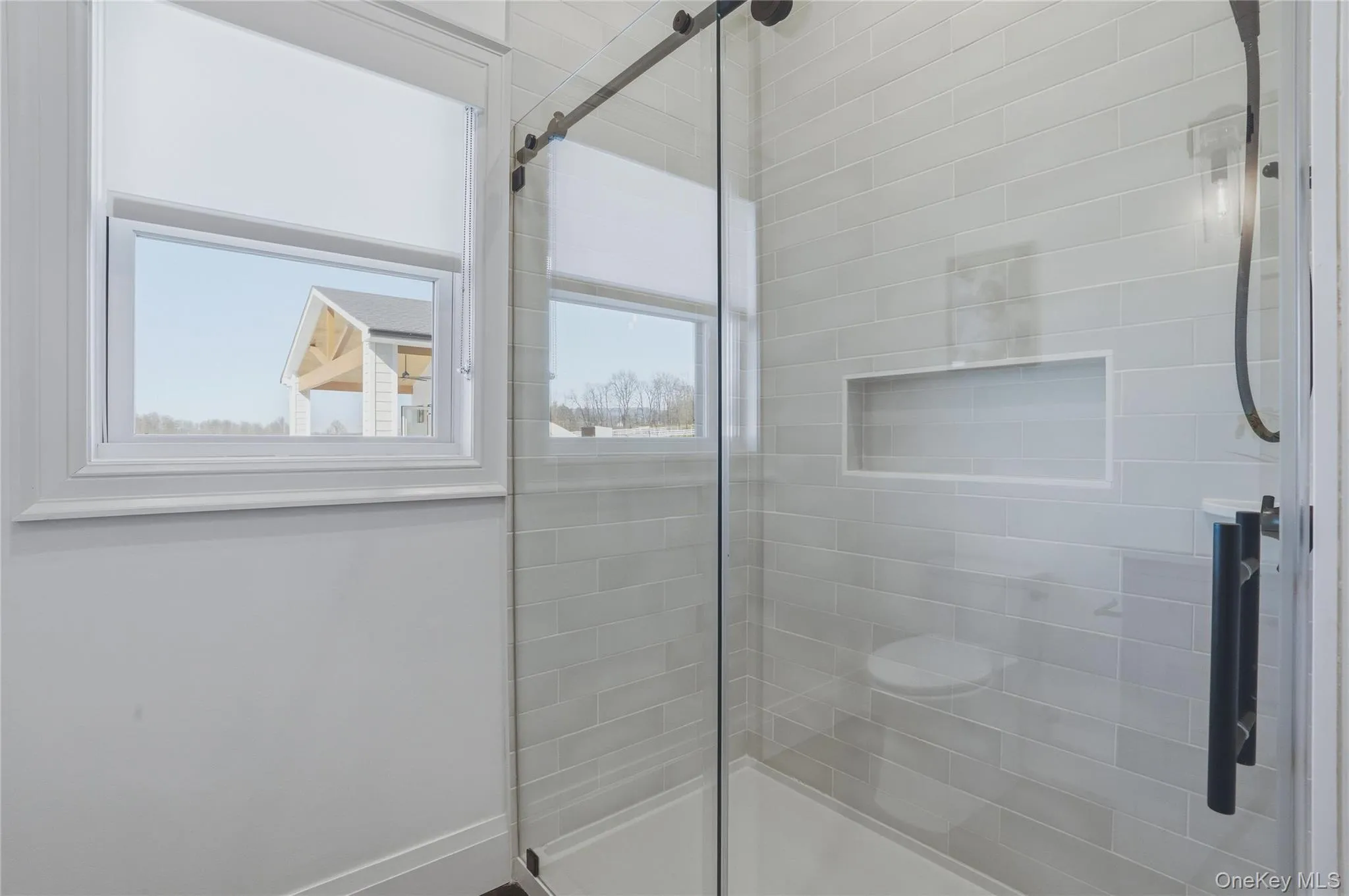 Modern shower enclosure featuring a sliding glass door, subway tile surround, built-in niche, and matte black hardware Modern shower enclosure featuring a sliding glass door, subway tile surround, built-in niche, and matte black hardware