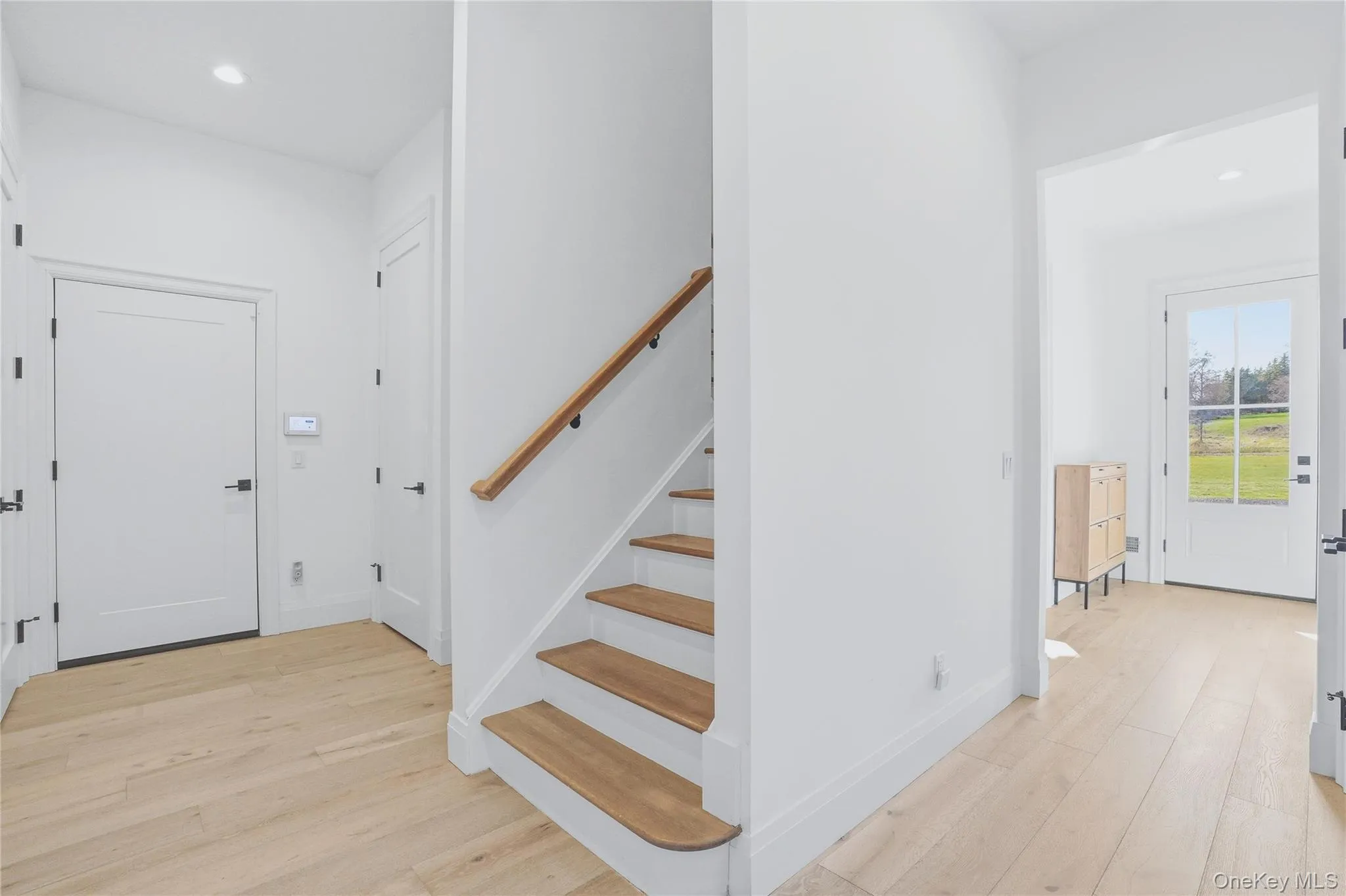 Foyer featuring light wood-finish flooring and a staircase with wood treads and handrail Foyer featuring light wood-finish flooring and a staircase with wood treads and handrail
