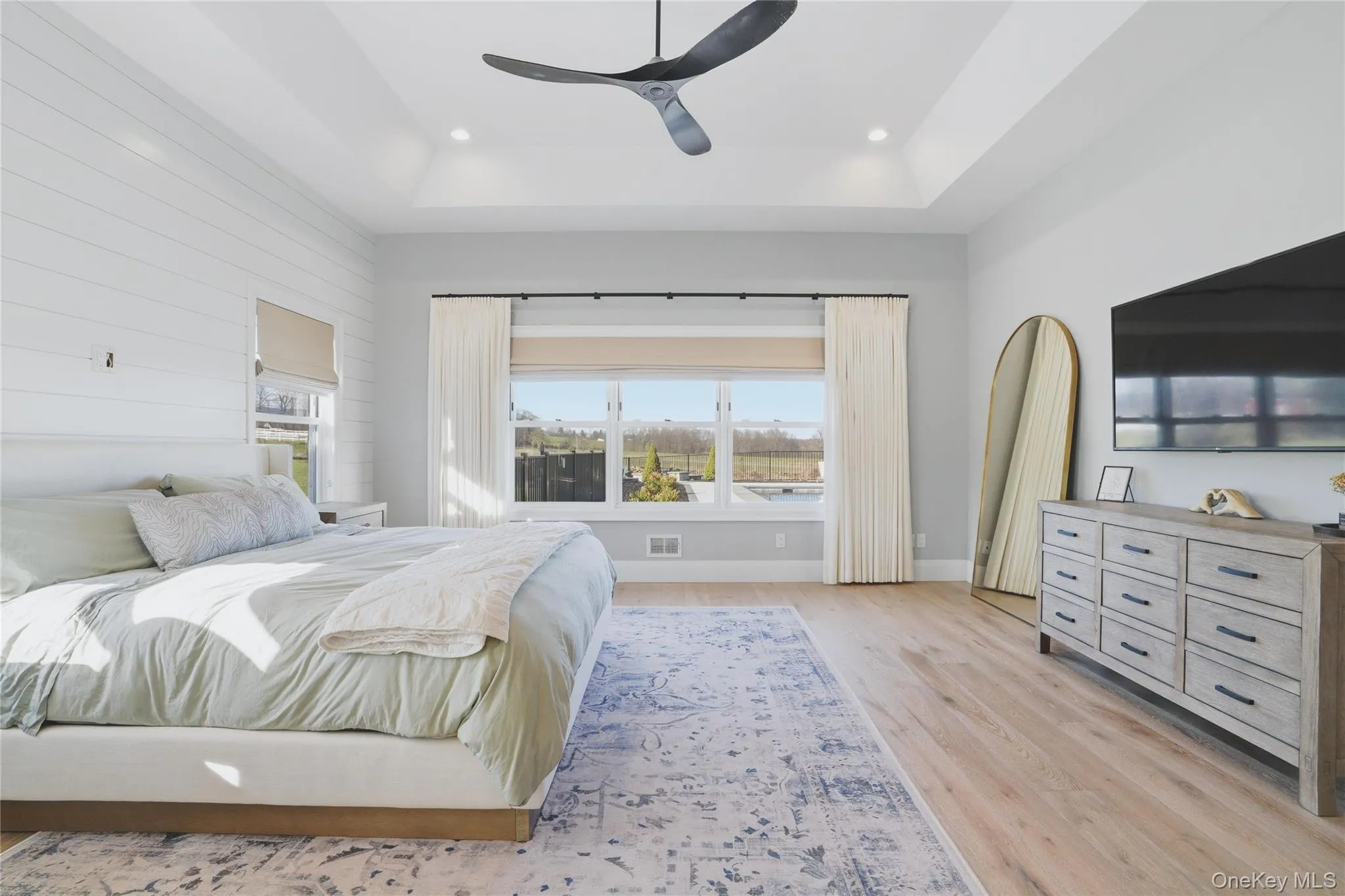 Spacious room featuring wood-finish flooring, a tray ceiling with recessed lighting, and a modern ceiling fan Spacious room featuring wood-finish flooring, a tray ceiling with recessed lighting, and a modern ceiling fan