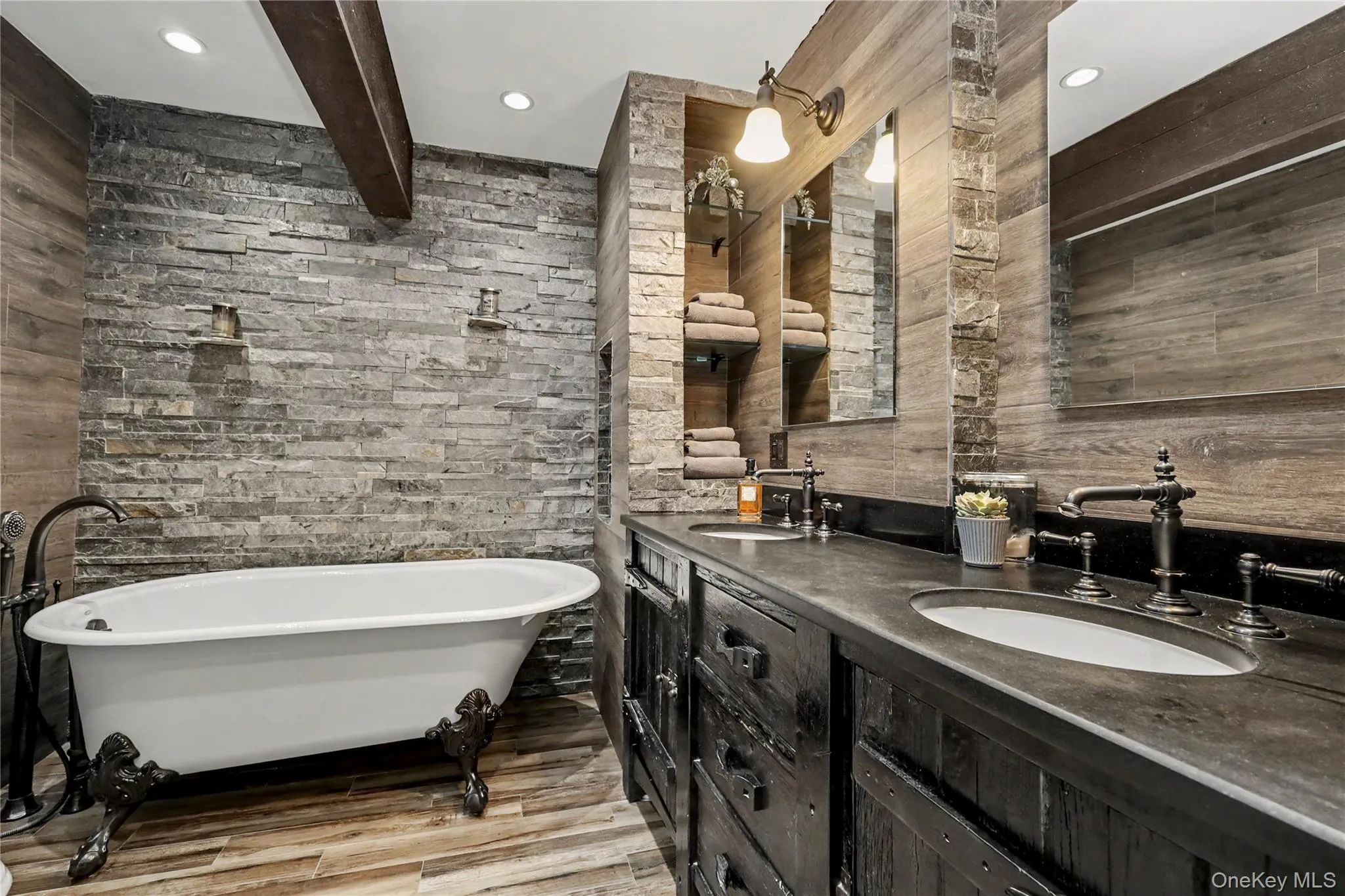 Rustic primary bathroom with clawfoot soaking tub and natural stone wall. Rustic primary bathroom with clawfoot soaking tub and natural stone wall.