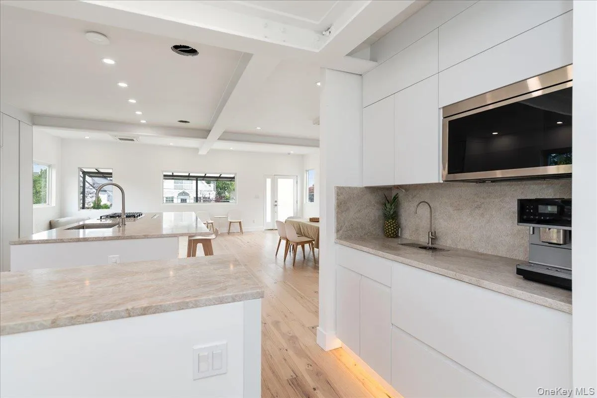 Kitchen featuring modern cabinets, stainless steel microwave, beam ceiling, light wood-type flooring, and a kitchen island with sink Kitchen featuring modern cabinets, stainless steel microwave, beam ceiling, light wood-type flooring, and a kitchen island with sink