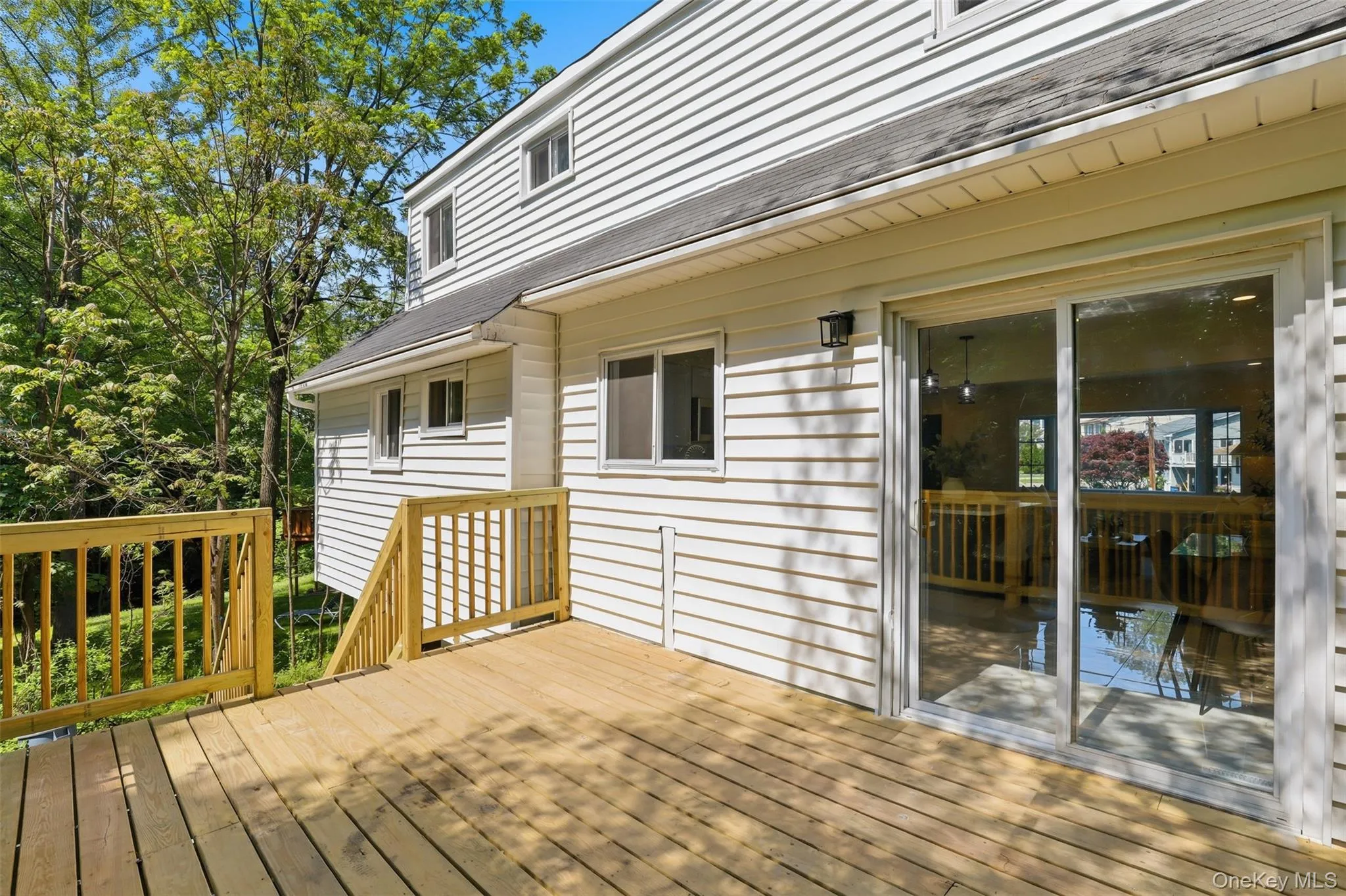 Expansive wooden deck with railing, featuring a sliding glass door entry to the interior, white horizontal siding, and multiple windows Expansive wooden deck with railing, featuring a sliding glass door entry to the interior, white horizontal siding, and multiple windows