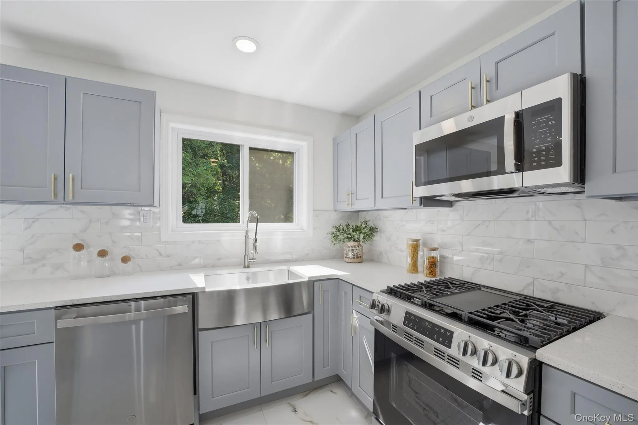 Contemporary kitchen featuring light gray cabinetry, stainless steel appliances, white countertops, and a white subway tile backsplash Contemporary kitchen featuring light gray cabinetry, stainless steel appliances, white countertops, and a white subway tile backsplash