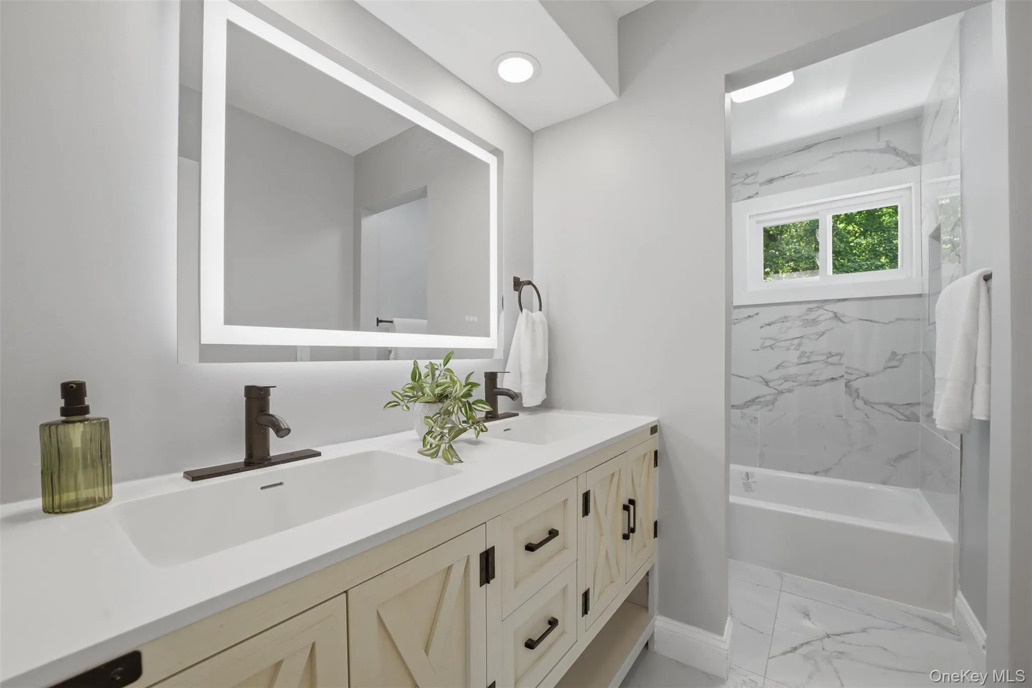 Main floor bathroom with dual vanity featuring a light wood-finish cabinet with dark hardware, a white countertop, and integrated sinks Main floor bathroom with dual vanity featuring a light wood-finish cabinet with dark hardware, a white countertop, and integrated sinks