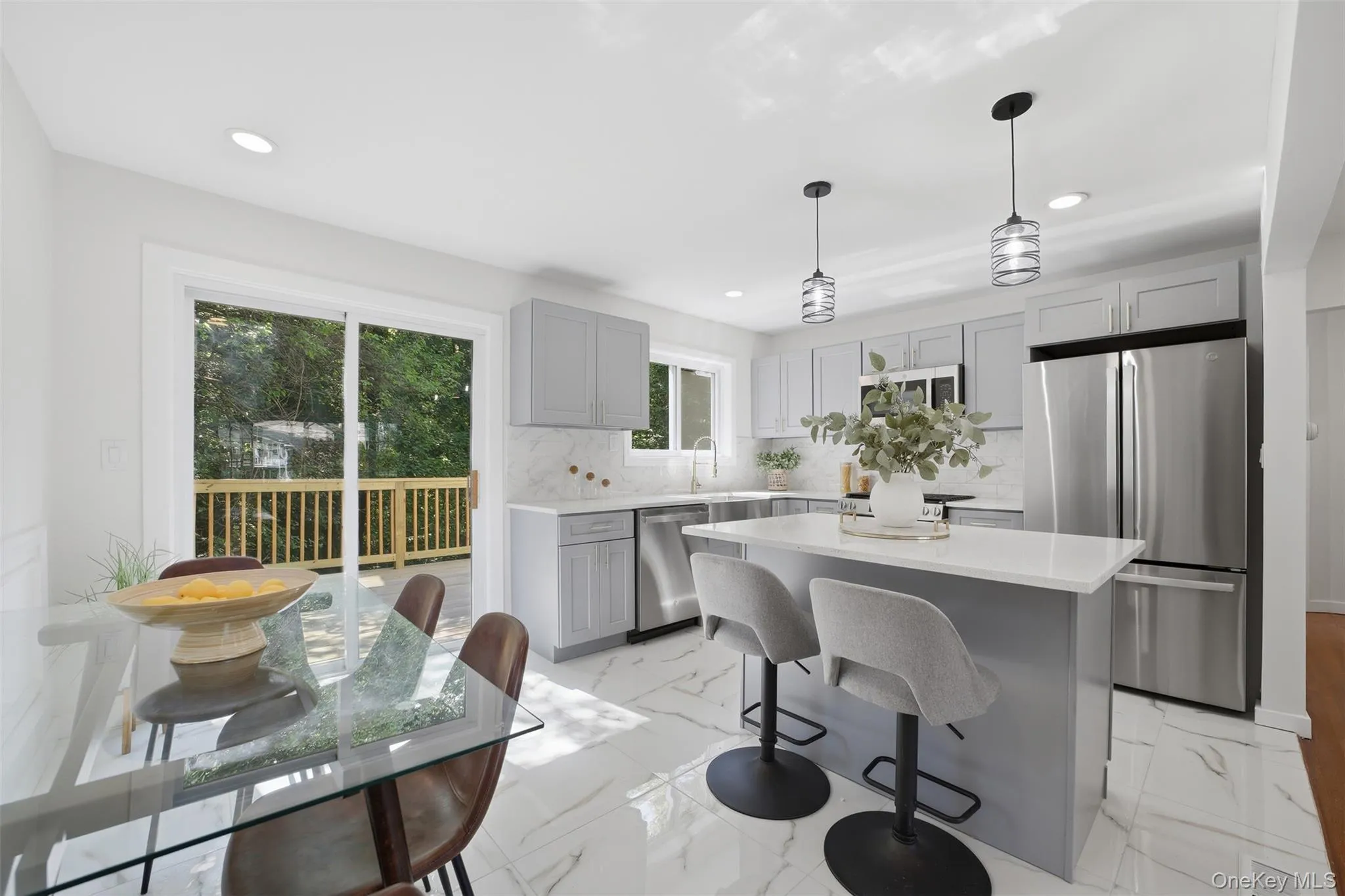 Modern kitchen featuring white marble-look flooring, light grey cabinetry, stainless steel appliances, and a central island with countertop seating Modern kitchen featuring white marble-look flooring, light grey cabinetry, stainless steel appliances, and a central island with countertop seating