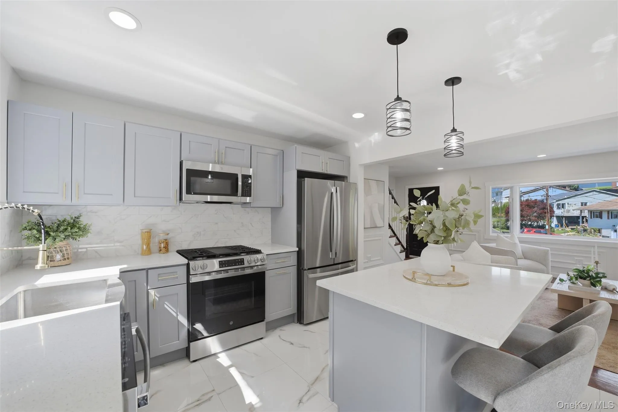 Open-concept kitchen featuring light-toned cabinetry, stainless steel appliances, a center island with pendant lighting, white countertops, and a full-height backsplash Open-concept kitchen featuring light-toned cabinetry, stainless steel appliances, a center island with pendant lighting, white countertops, and a full-height backsplash