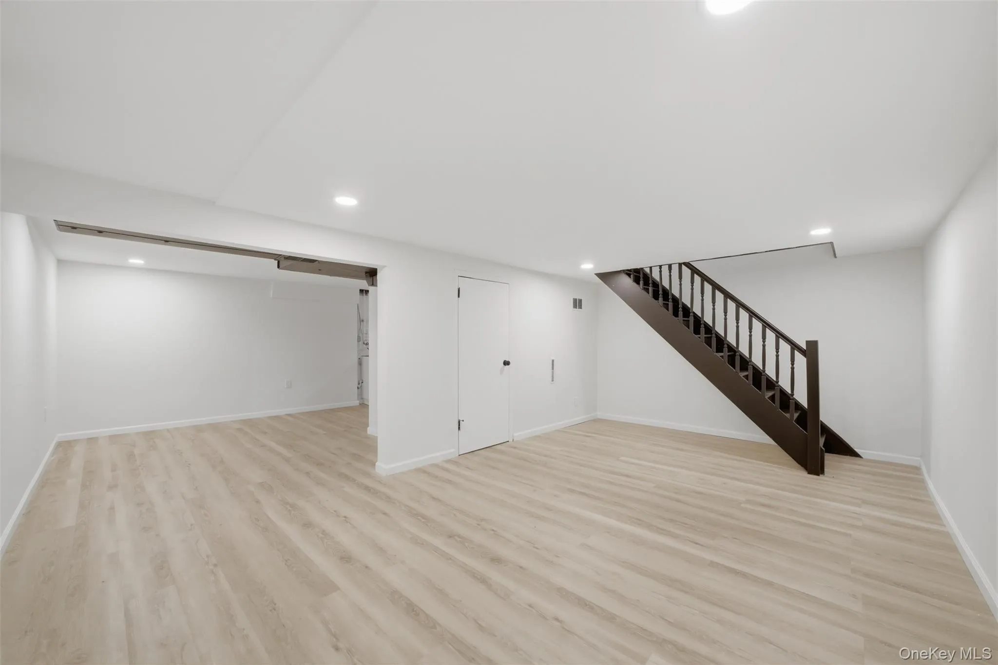 Spacious open finished basement featuring light wood-finish flooring, recessed lighting, and a dark wood staircase Spacious open finished basement featuring light wood-finish flooring, recessed lighting, and a dark wood staircase