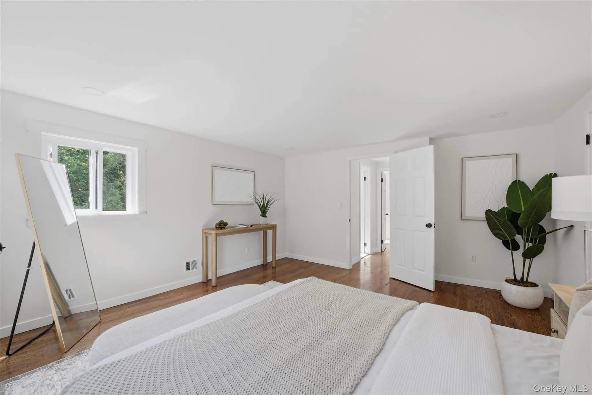 Spacious primary bedroom on top floor featuring wood-finish flooring, white walls, and a window with exterior views Spacious primary bedroom on top floor featuring wood-finish flooring, white walls, and a window with exterior views