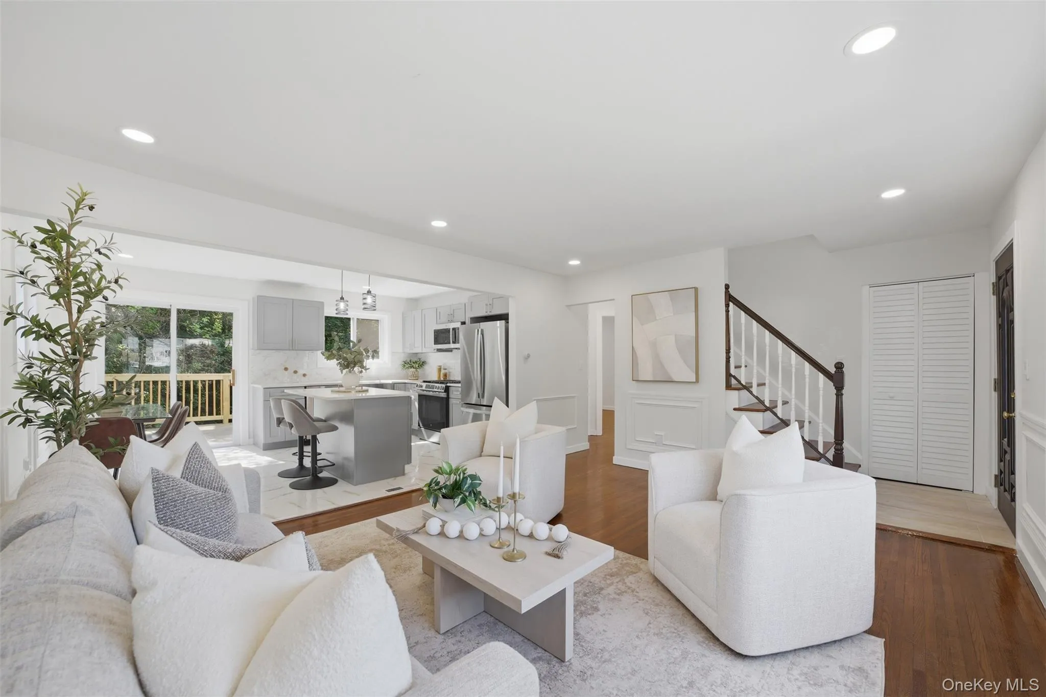 Bright living area featuring wood-finish flooring, recessed lighting, and a staircase with white risers and a dark wood handrail Bright living area featuring wood-finish flooring, recessed lighting, and a staircase with white risers and a dark wood handrail