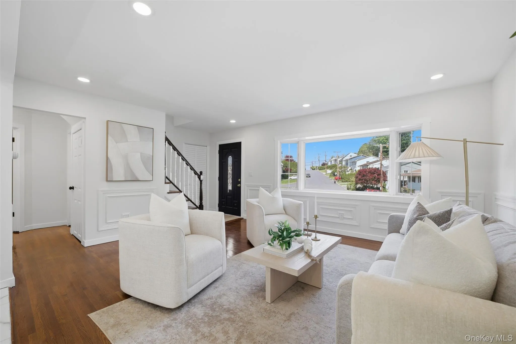 Bright living space featuring hardwood flooring, recessed lighting, expansive front window, decorative wall molding, and a dark wood-finish entry door with glass inserts Bright living space featuring hardwood flooring, recessed lighting, expansive front window, decorative wall molding, and a dark wood-finish entry door with glass inserts