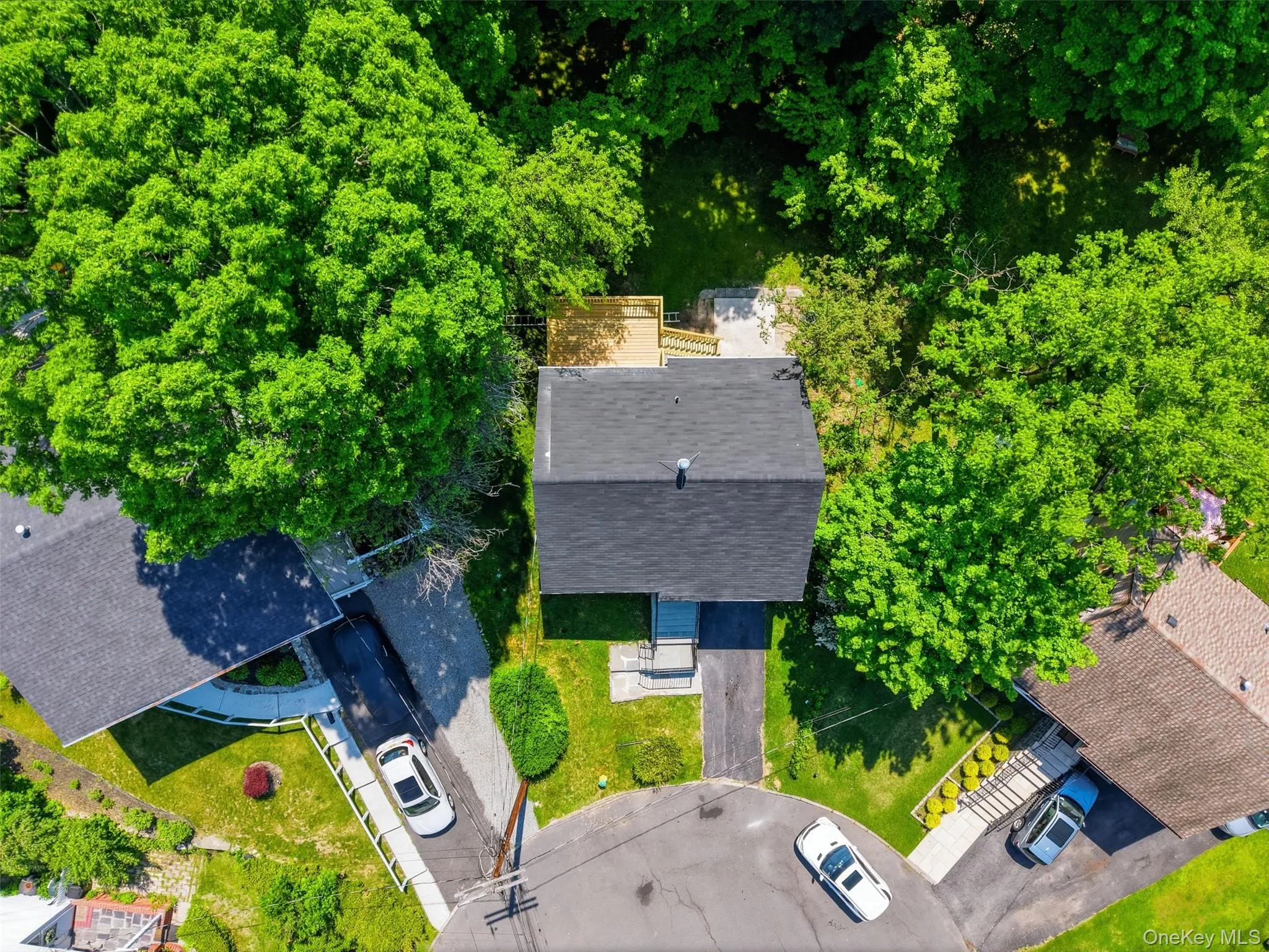 Aerial perspective of a property featuring a central residence with a dark shingle roof, surrounded by mature green trees Aerial perspective of a property featuring a central residence with a dark shingle roof, surrounded by mature green trees
