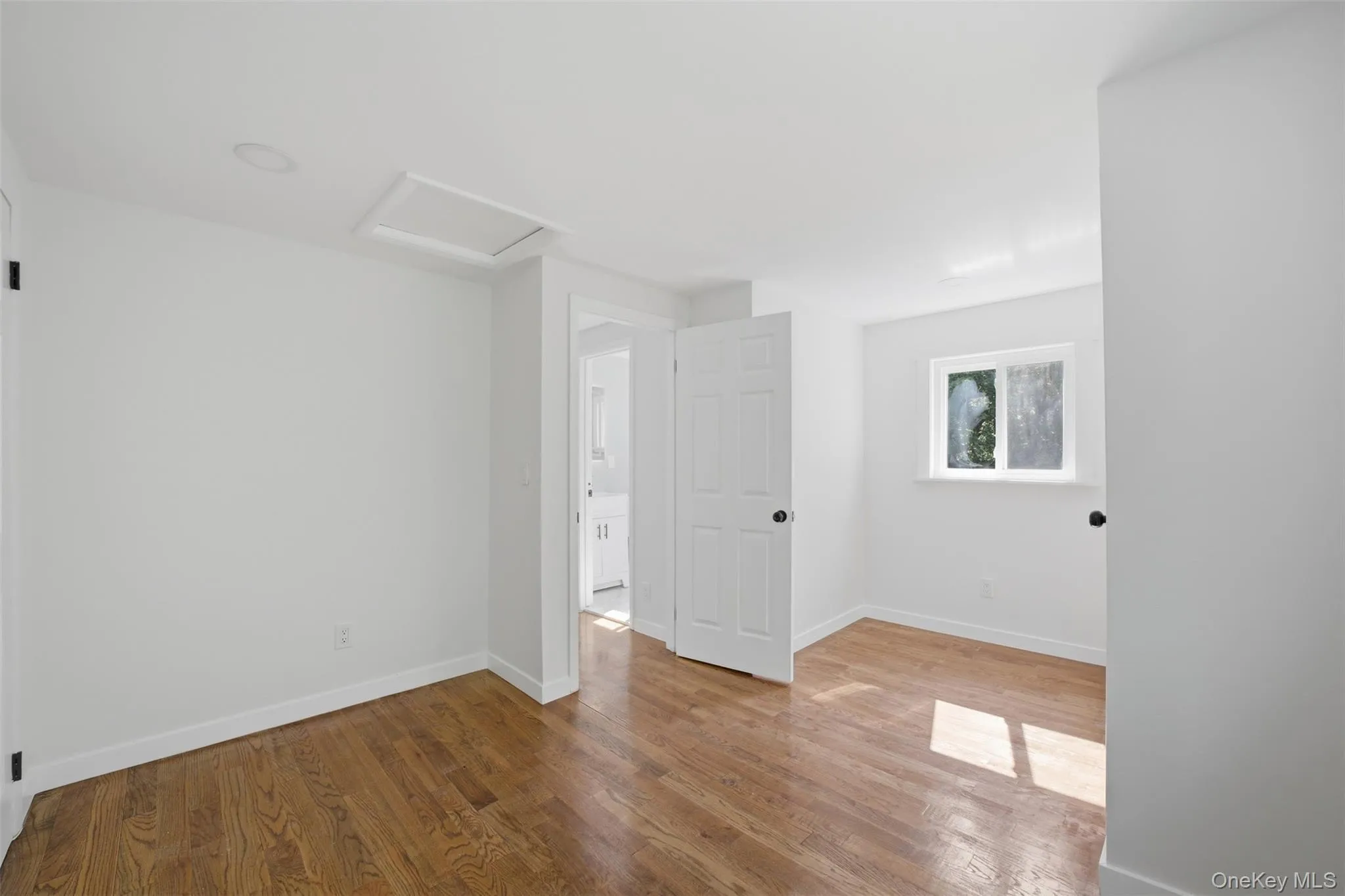 Bright top floor bedroom featuring wood-finish flooring, white walls, and a white trim Bright top floor bedroom featuring wood-finish flooring, white walls, and a white trim
