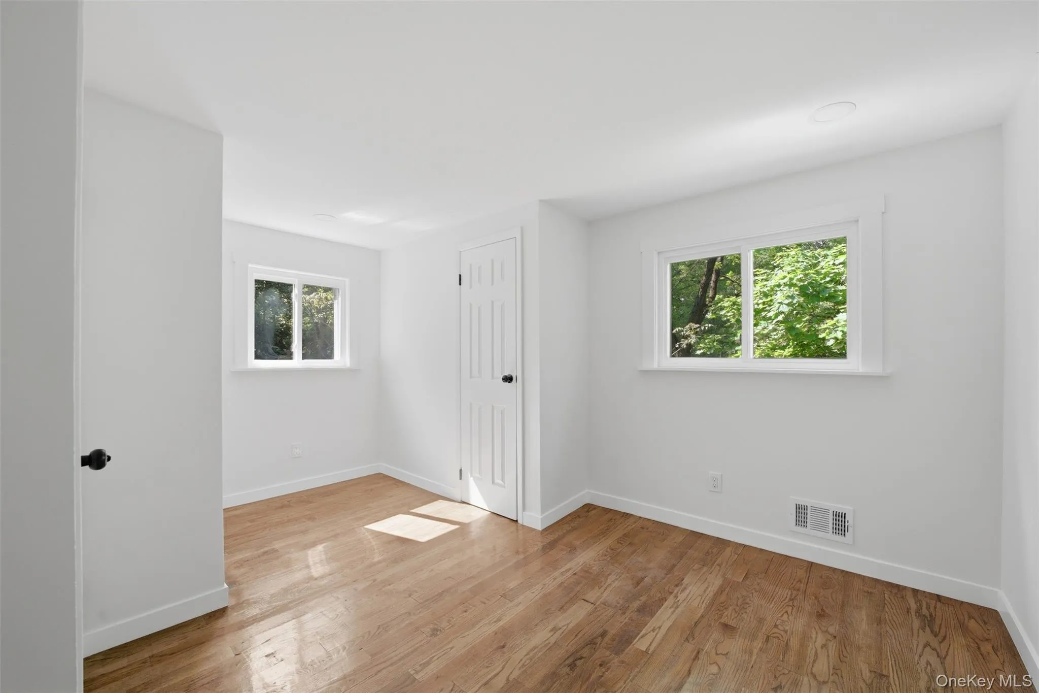 Bright top floor bedroom featuring wood-finish flooring, white walls, and two windows with white trim Bright top floor bedroom featuring wood-finish flooring, white walls, and two windows with white trim