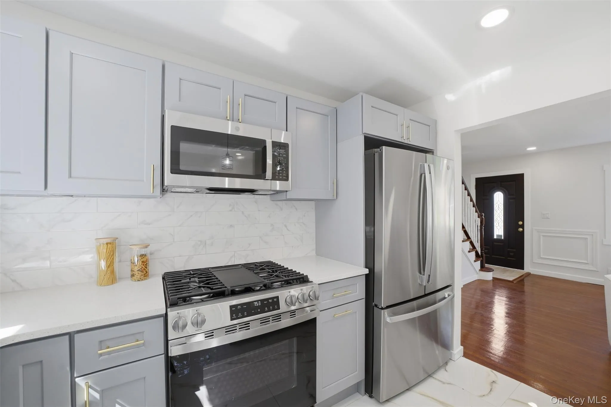 Modern kitchen featuring light gray cabinetry with gold-tone hardware, stainless steel appliances, a white subway tile backsplash, and white countertops Modern kitchen featuring light gray cabinetry with gold-tone hardware, stainless steel appliances, a white subway tile backsplash, and white countertops