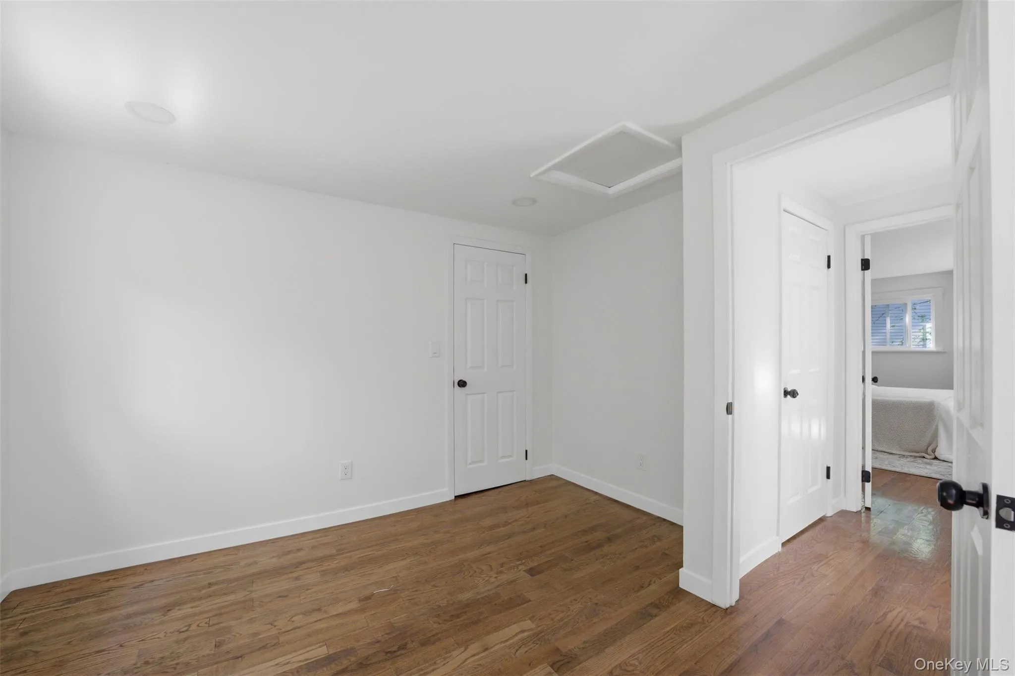Top floor bedroom with wood-finish flooring throughout, white baseboards, recessed ceiling lighting, and a white paneled door with a black doorknob Top floor bedroom with wood-finish flooring throughout, white baseboards, recessed ceiling lighting, and a white paneled door with a black doorknob