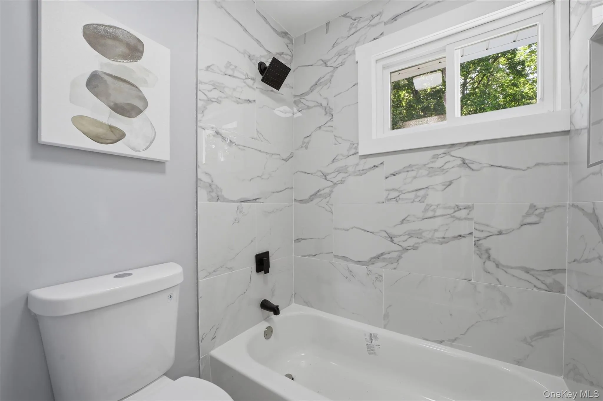 Main Floor bathroom featuring a white porcelain tub with matte black fixtures, surrounded by large format marble-look tile Main Floor bathroom featuring a white porcelain tub with matte black fixtures, surrounded by large format marble-look tile