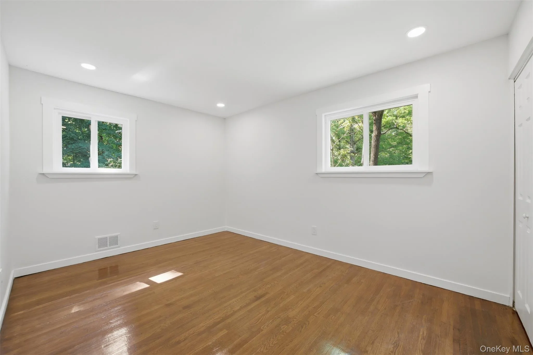 2nd main floor bedroom featuring hardwood flooring provides a warm foundation for this neutral room, featuring recessed lighting, white baseboards, and two windows with white trim 2nd main floor bedroom featuring hardwood flooring provides a warm foundation for this neutral room, featuring recessed lighting, white baseboards, and two windows with white trim