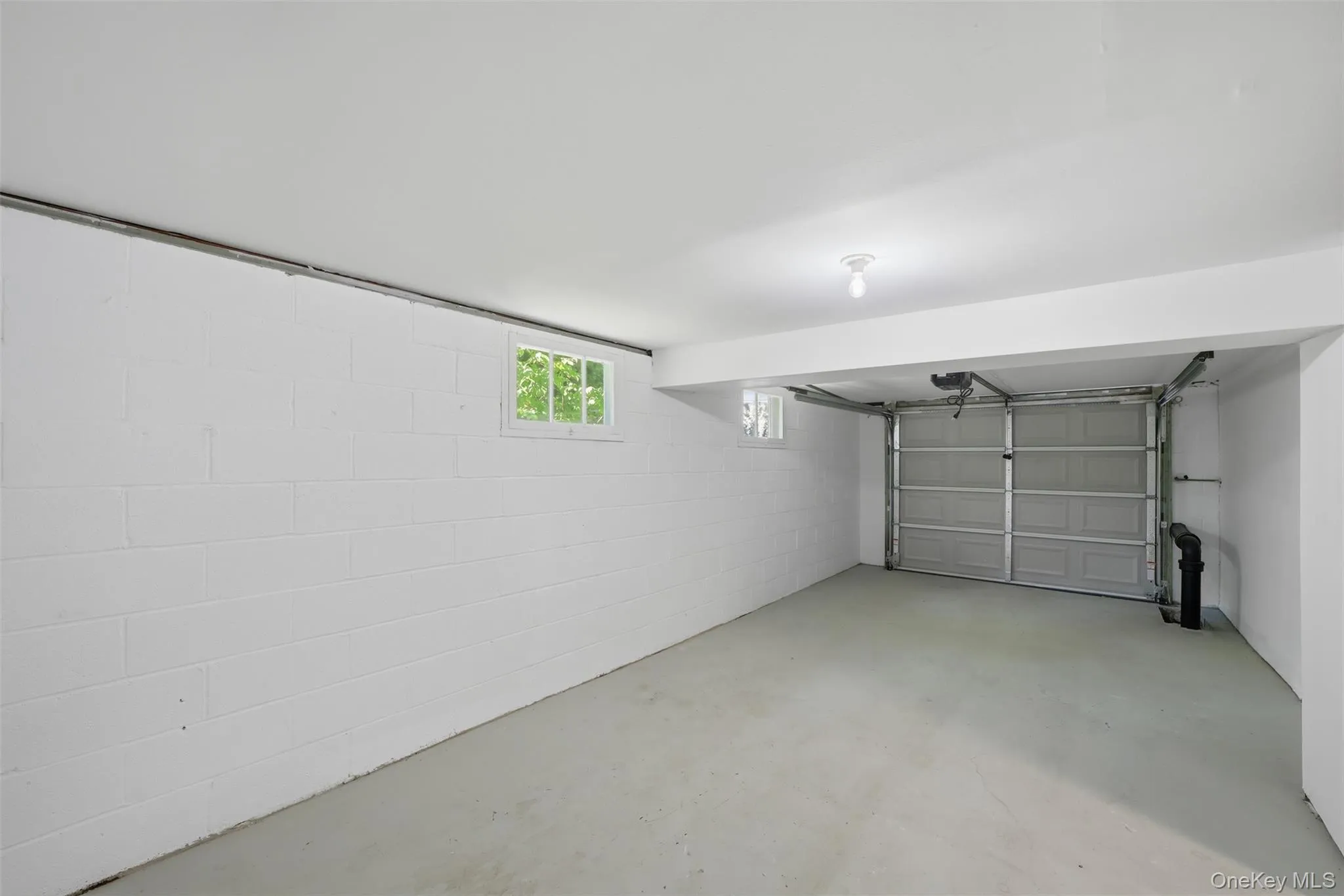 Spacious garage featuring a concrete floor, painted cinder block walls, and a single overhead garage door Spacious garage featuring a concrete floor, painted cinder block walls, and a single overhead garage door
