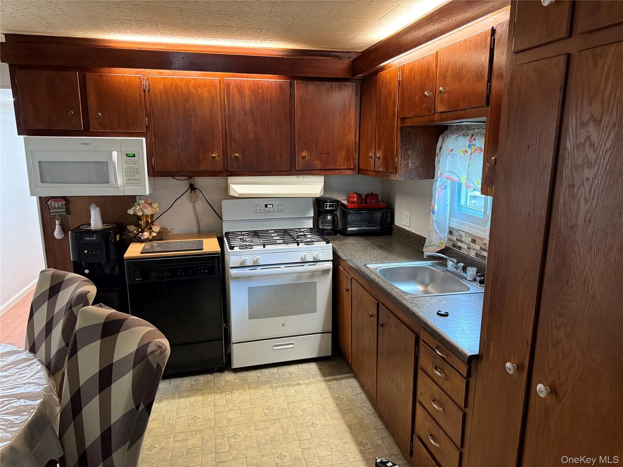 Kitchen featuring wood cabinetry, laminate countertops, a stainless steel sink, and a tile backsplash Kitchen featuring wood cabinetry, laminate countertops, a stainless steel sink, and a tile backsplash
