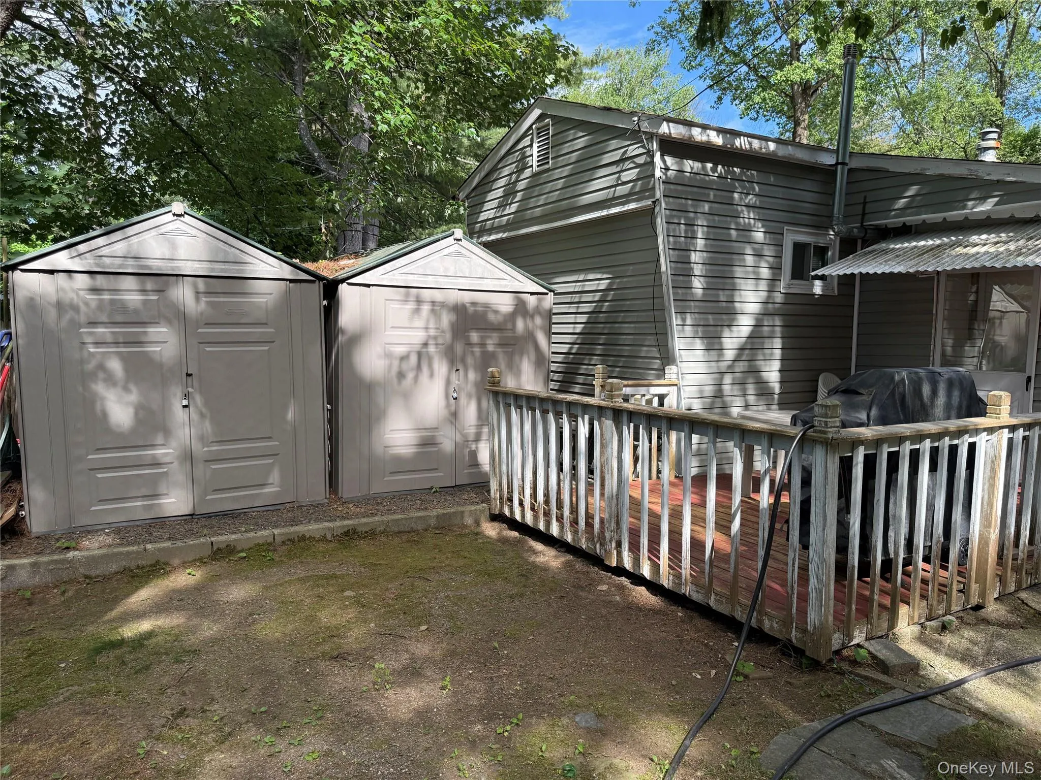 Rear exterior featuring a wood deck with railing and two detached storage sheds on a gravel base Rear exterior featuring a wood deck with railing and two detached storage sheds on a gravel base
