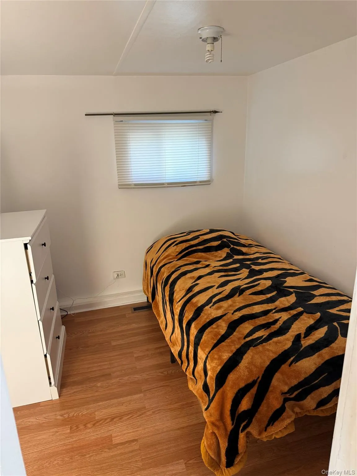Bedroom 2 featuring wood-finish flooring, a single window with horizontal blinds, and a flush-mount ceiling light fixture Bedroom 2 featuring wood-finish flooring, a single window with horizontal blinds, and a flush-mount ceiling light fixture