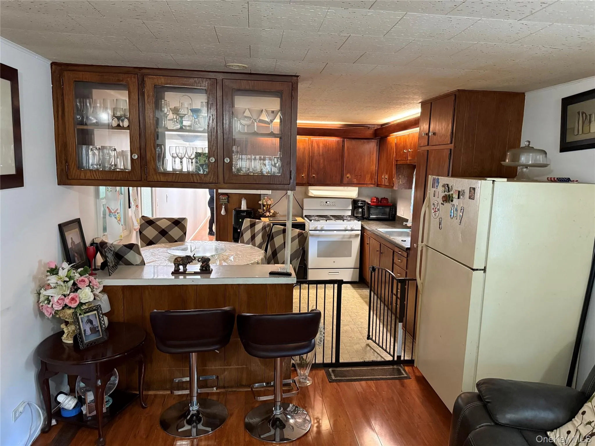 Kitchen featuring wood-finish cabinetry, a white gas range, and a breakfast bar with built-in overhead glass-front cabinets Kitchen featuring wood-finish cabinetry, a white gas range, and a breakfast bar with built-in overhead glass-front cabinets